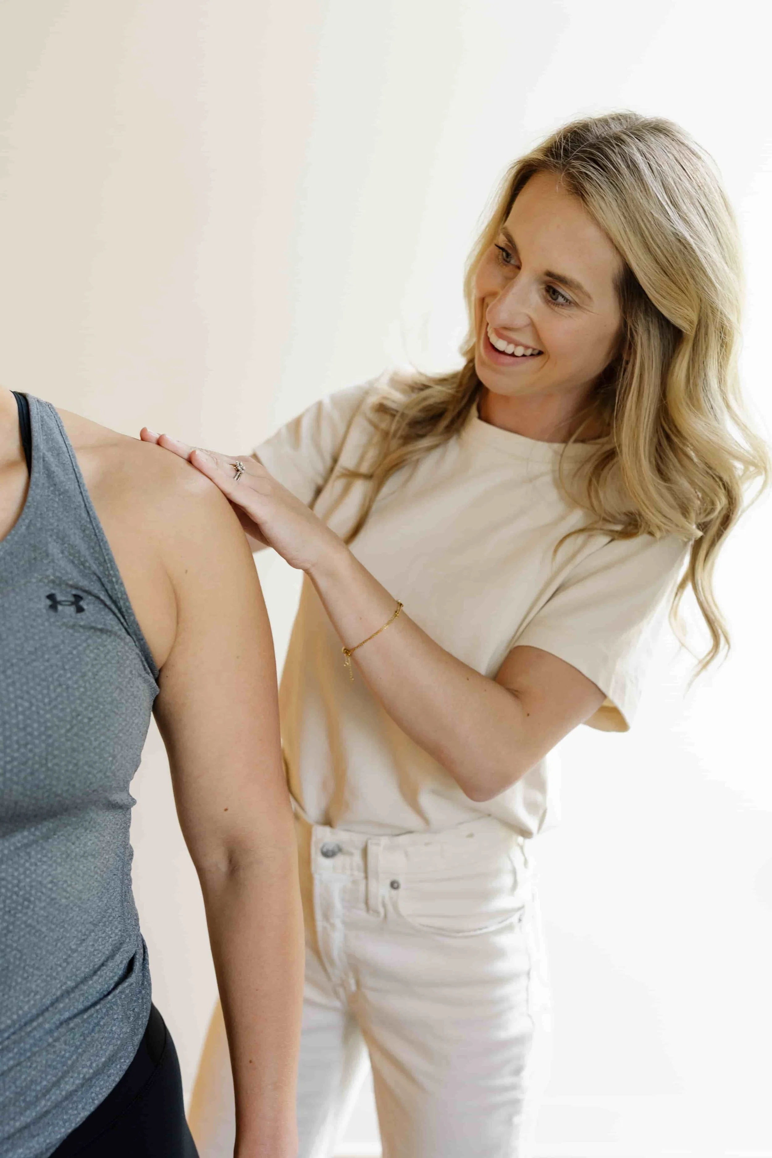 A woman smiling and touching a person's shoulder in a clinical setting.