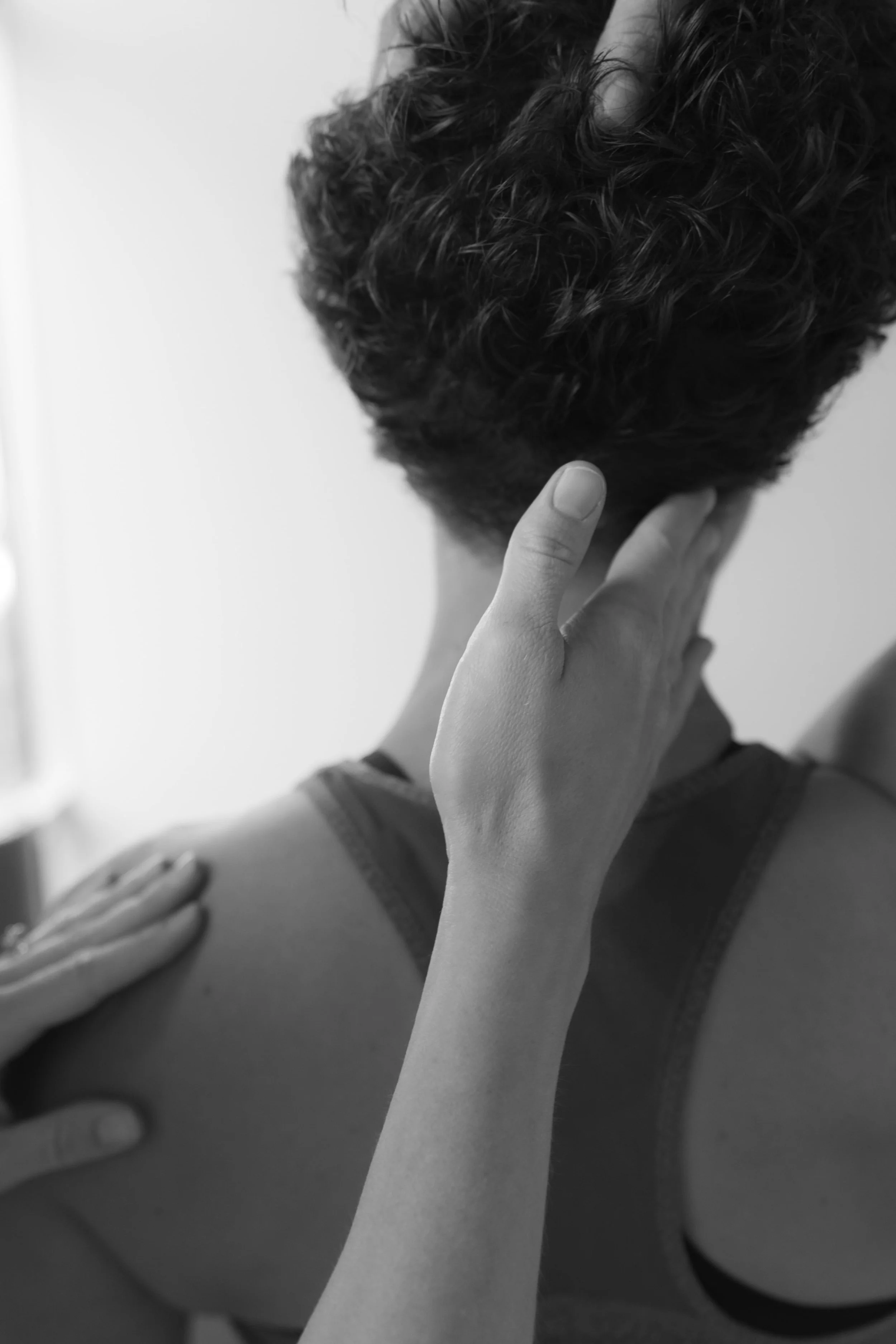 A person receiving a massage on their shoulder, with their hand touching the back of their neck and another hand helping.