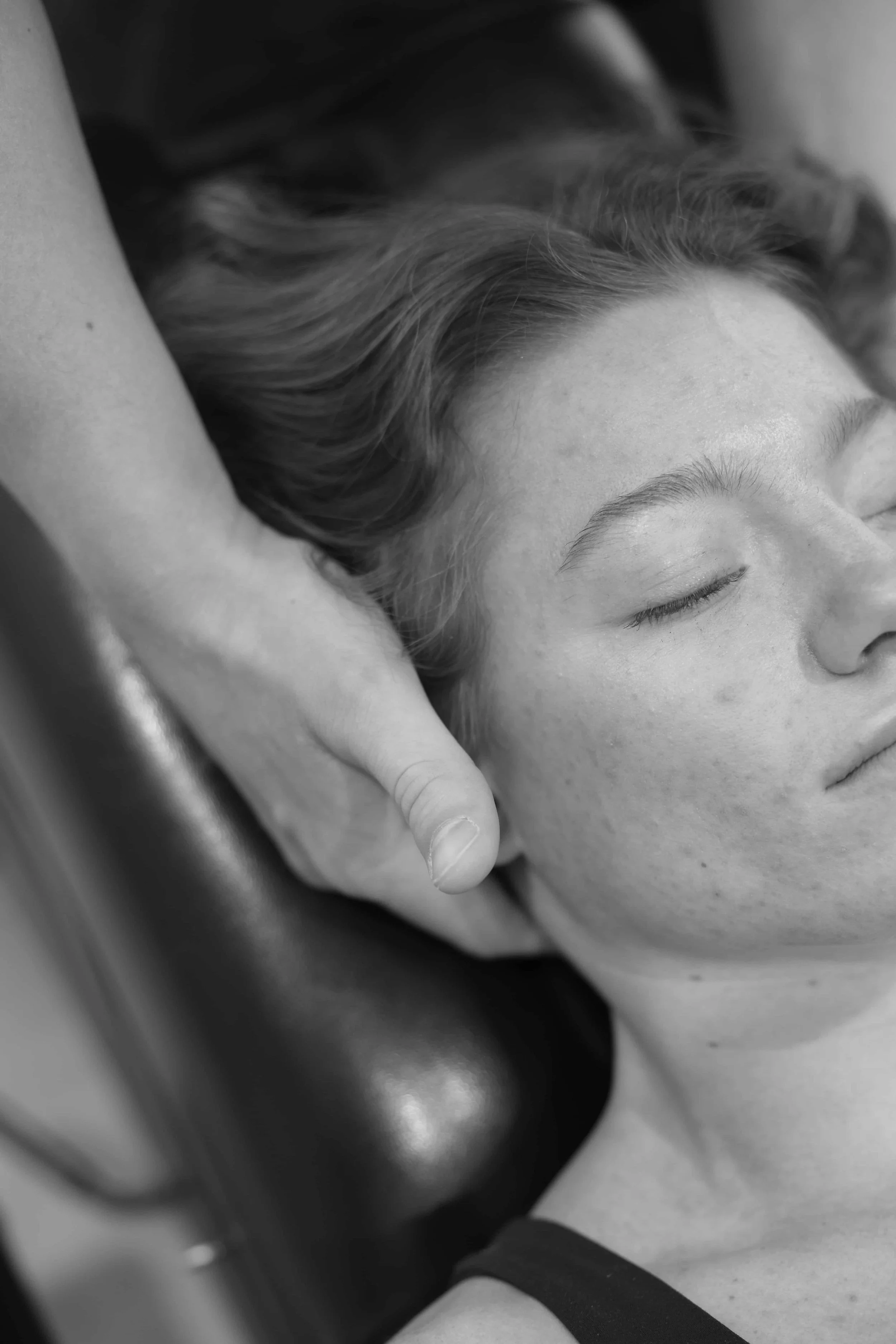 A woman receiving a chiropractic adjustment while lying down, eyes closed, with a chiropractor's hand on her neck.