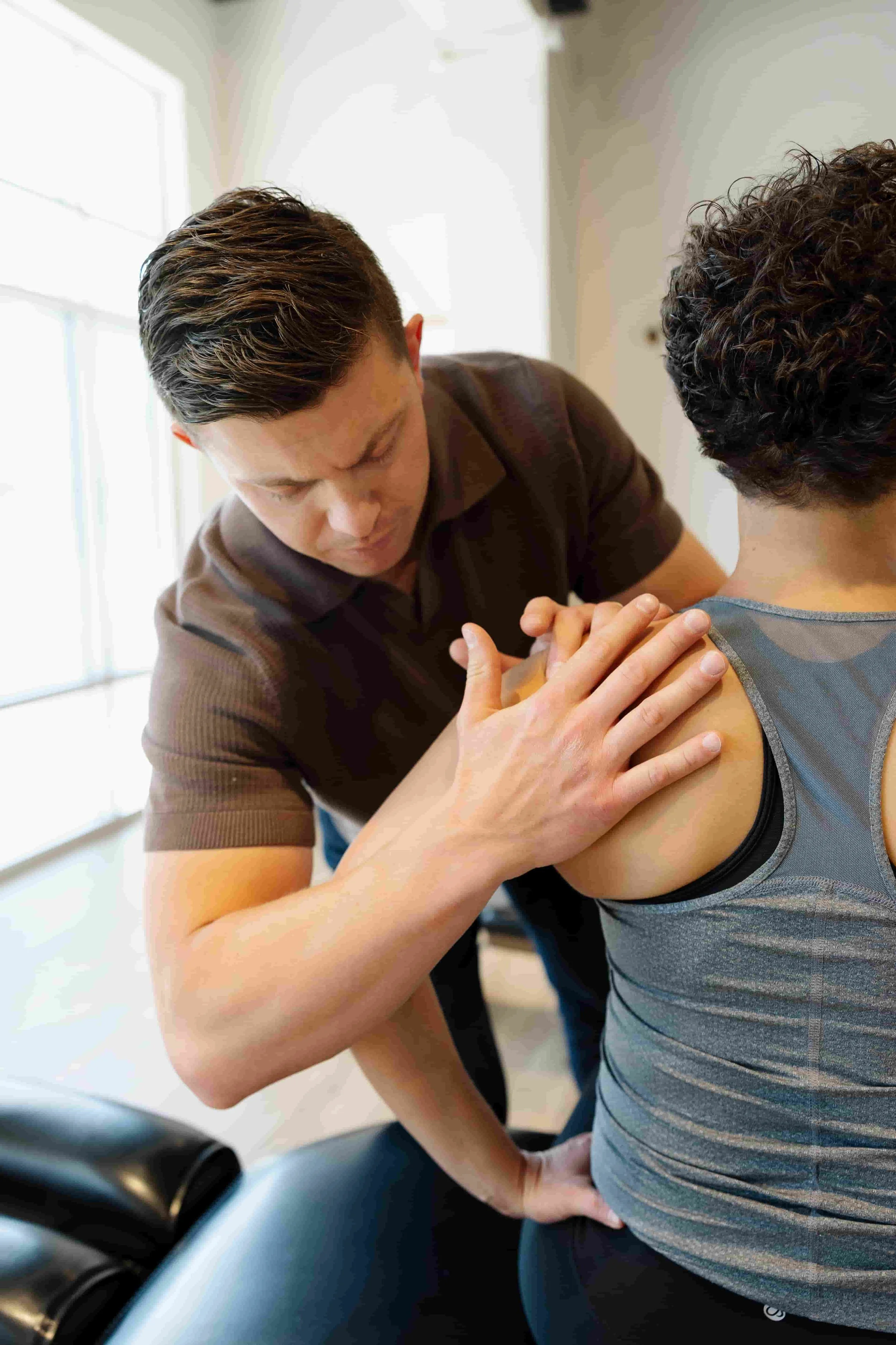 Physical therapist examining a woman's shoulder in a clinical setting.