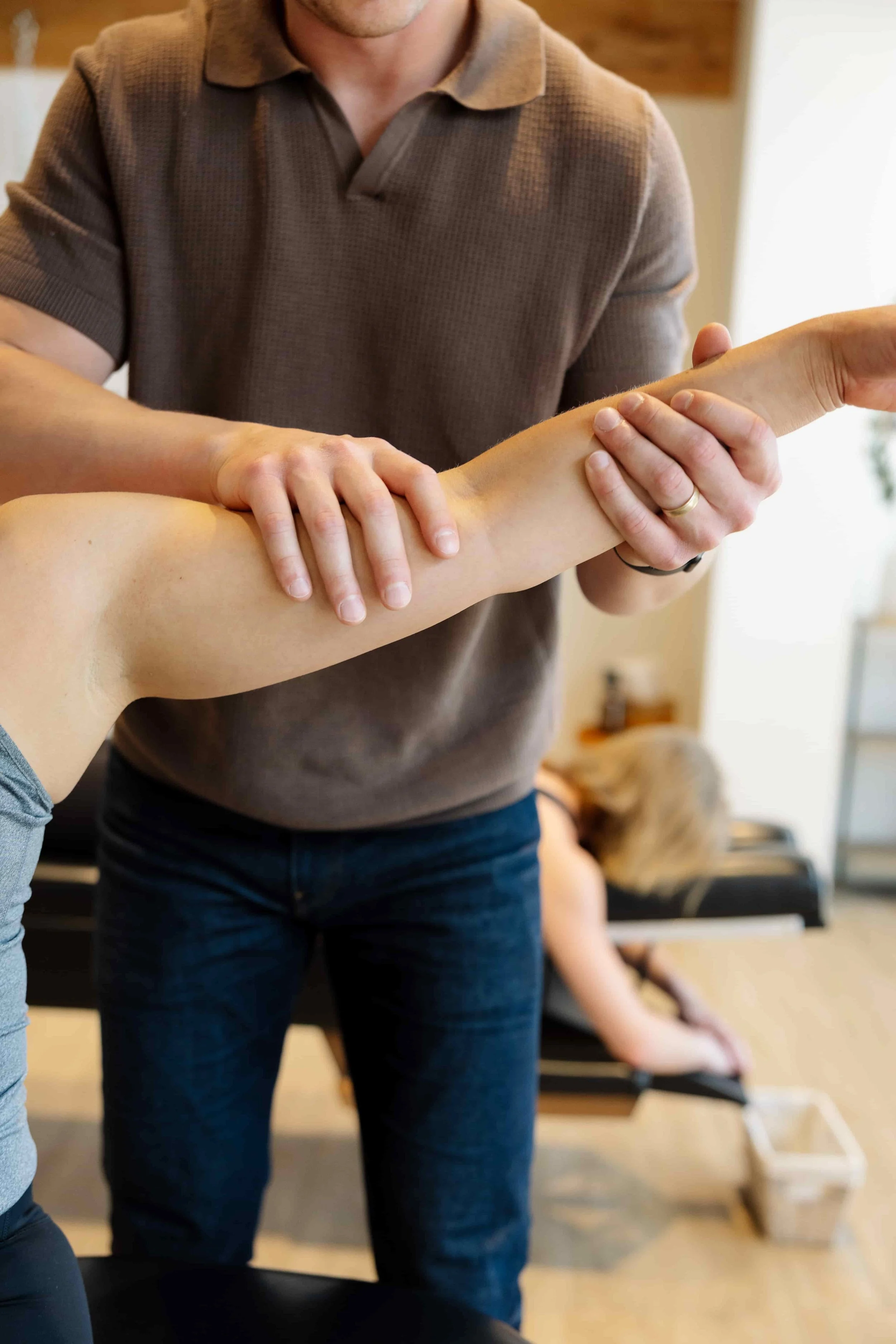 A person receiving a physical therapy or chiropractic adjustment on their arm from a therapist in a room with furniture and a dog in the background.