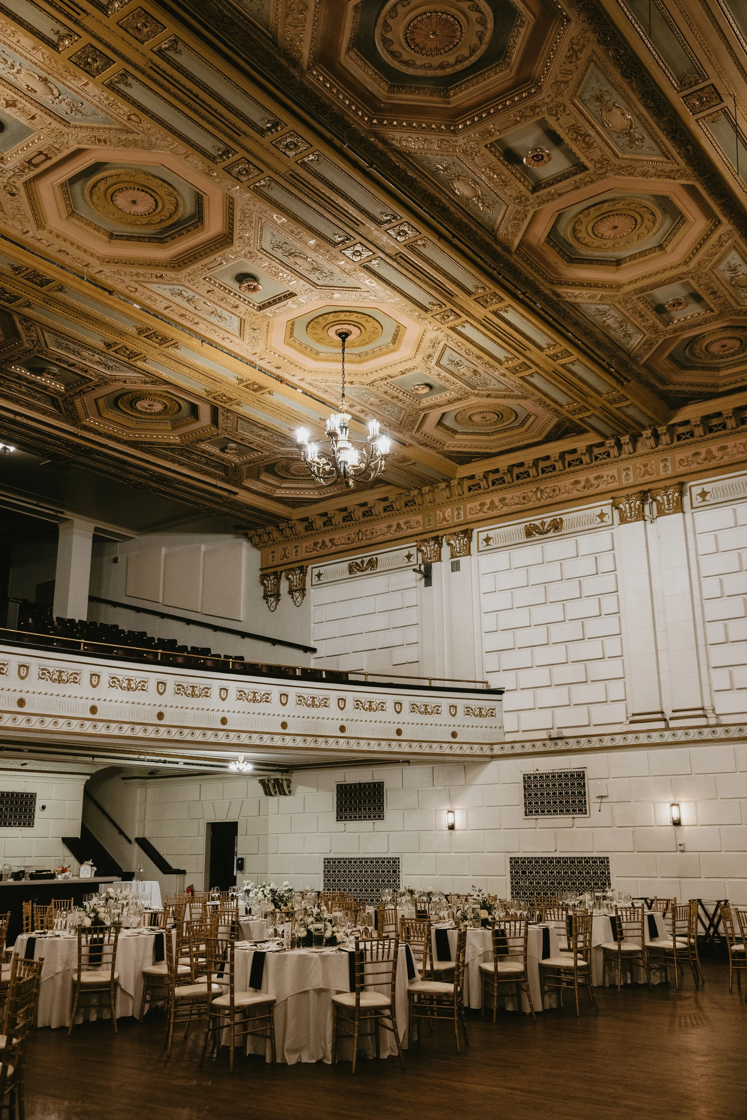 Elegant banquet hall with ornate gold and white ceiling, chandelier, and round tables set for a formal event.