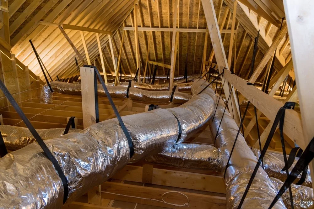 Insulated HVAC ductwork installed in an attic with wooden framing and sloped roof