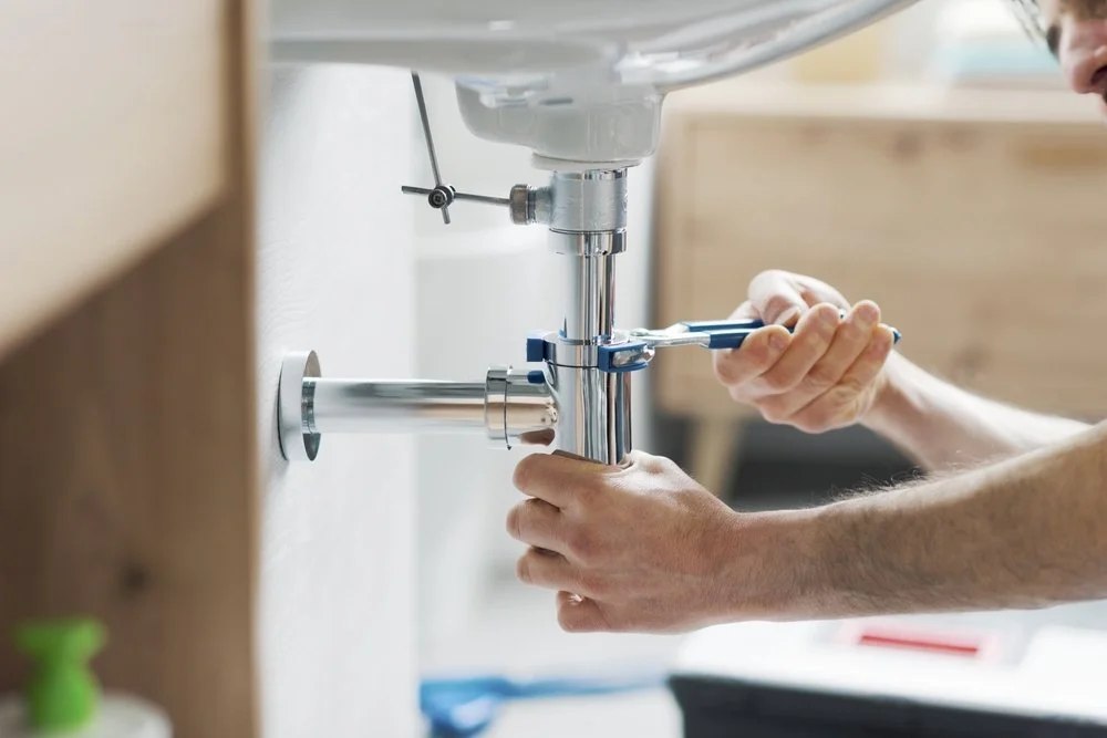 Person connecting or repairing a plumbing pipe under a sink in a kitchen.