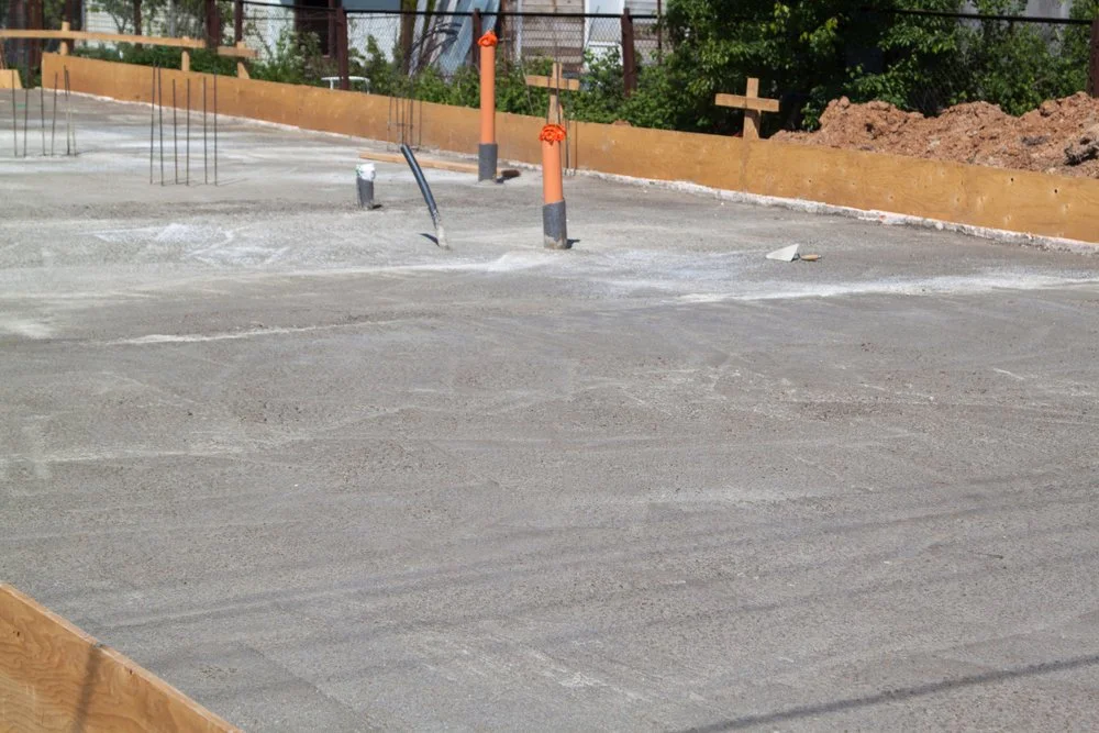Concrete foundation in a construction site with orange safety pipes, rebar, and wooden borders.