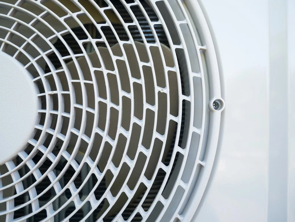 Close-up of a white circular air vent or fan grill in a white surface.