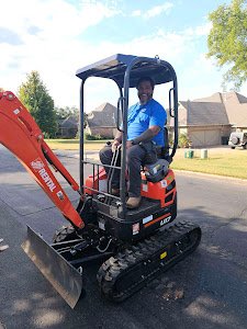 Man operating a small orange excavator on a residential street.
