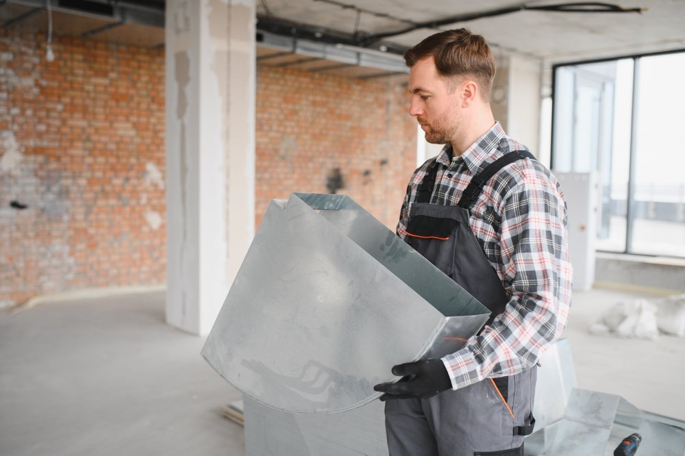 Man inspecting a metal duct in an unfinished building under construction.