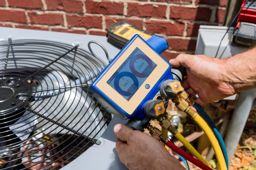 Technician measures HVAC system's refrigerant pressure with gauge in outdoor unit.