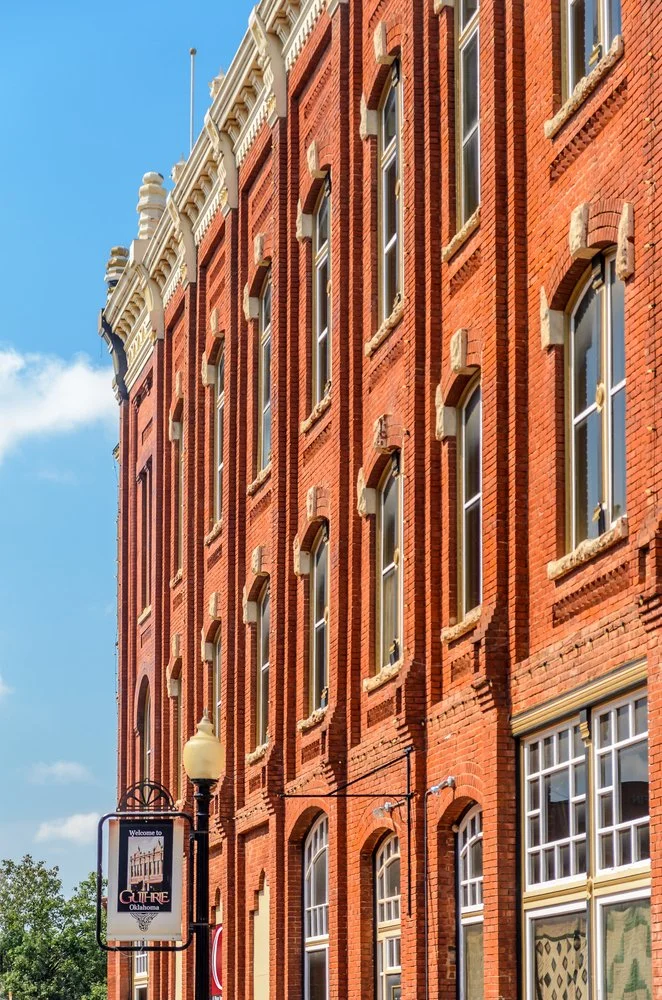 Red brick historic building with multiple tall windows and ornate architectural details, under a blue sky, in Oklahoma.