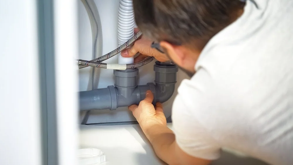 A person working under a sink, fixing or inspecting the plumbing pipes.