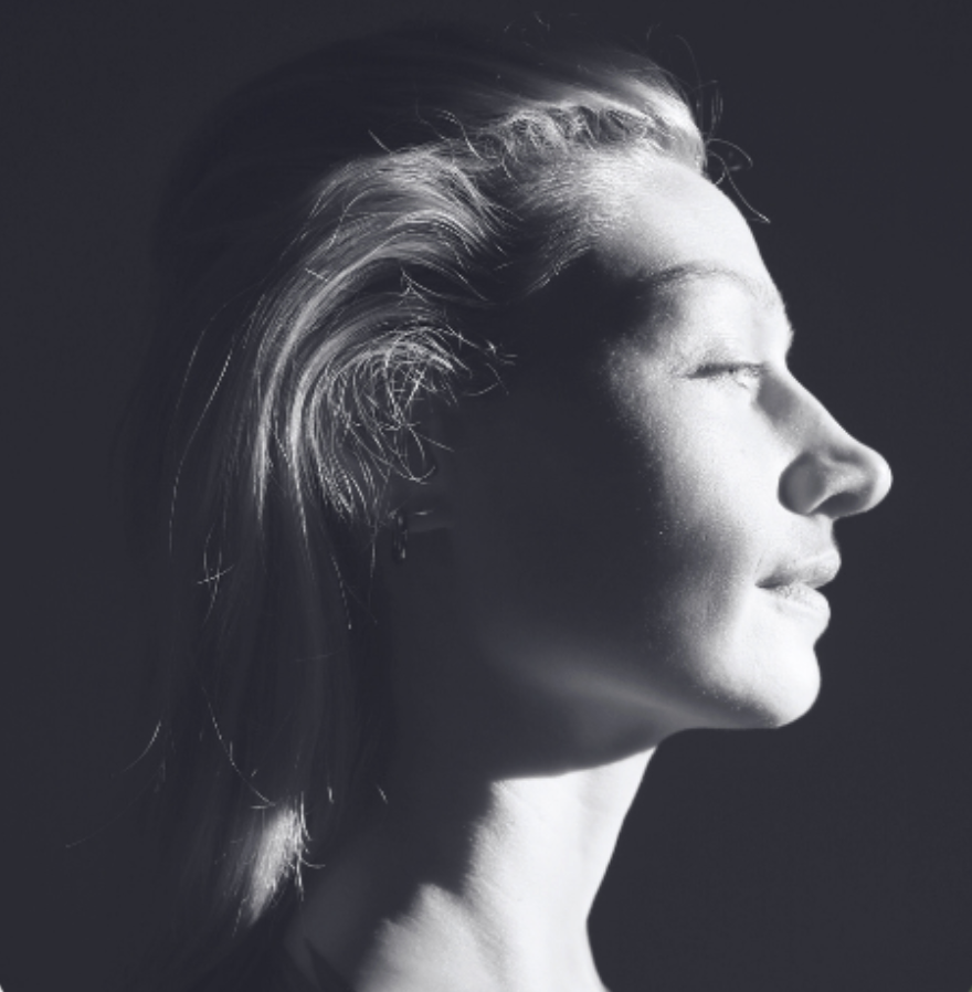 Black and white photo of a woman with her eyes closed, her face illuminated by soft light, showing a serene expression.