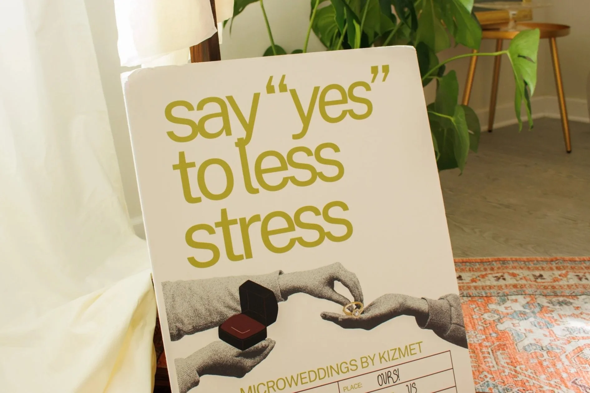 A sign encouraging people to 'say yes to less stress' with a graphic of a hand passing a ring to another hand, symbolizing a wedding vow, at a Microweddings event by Kizmet.