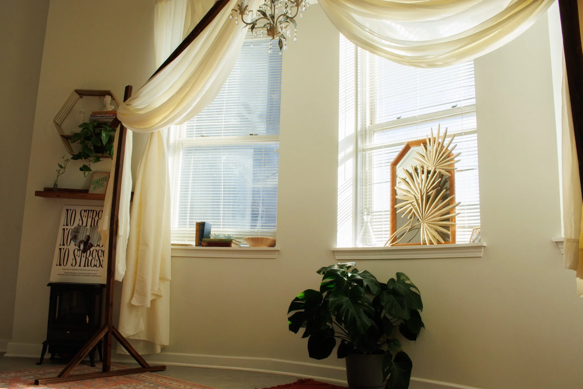 Bright room with large windows, sheer curtains, houseplants, decorative objects, and a chandelier.