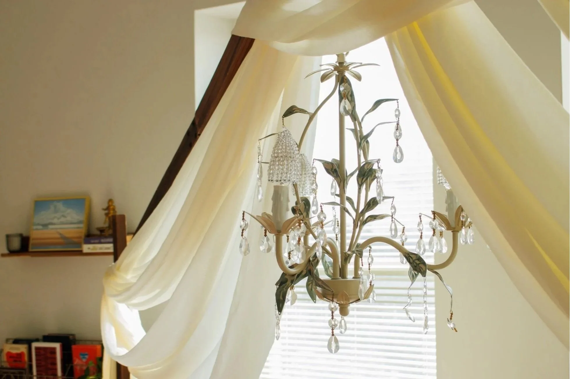 Chandelier designed as a tree with leaves and hanging crystal ornaments, hanging in a room with yellow curtains and window blinds.