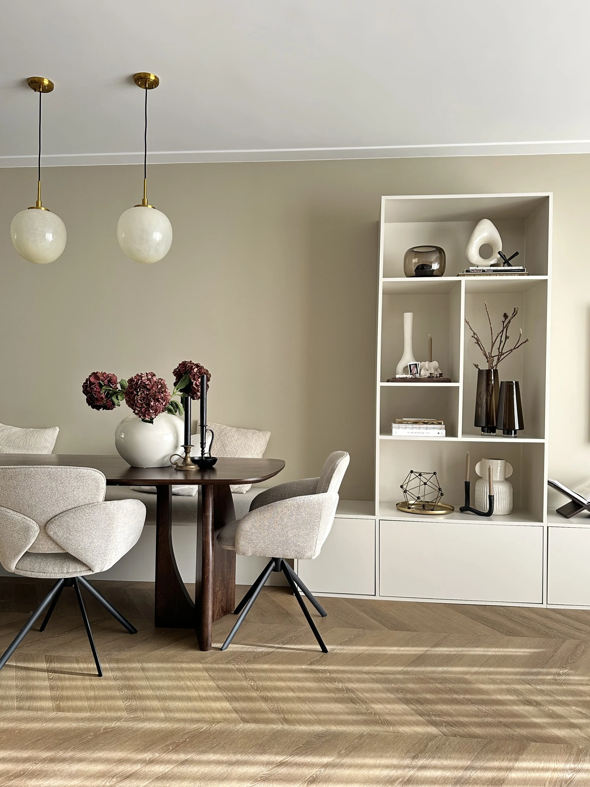 Moderne eetkamer hoek met beige eetkamerstoelen, een houten tafel, vakkenkast en decoratieve items.
