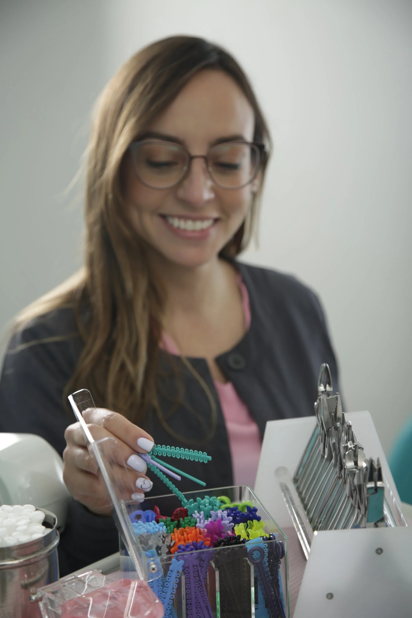 Mujer sonriendo mientras selecciona juguetes para uñas de una caja transparente en un salón de belleza.