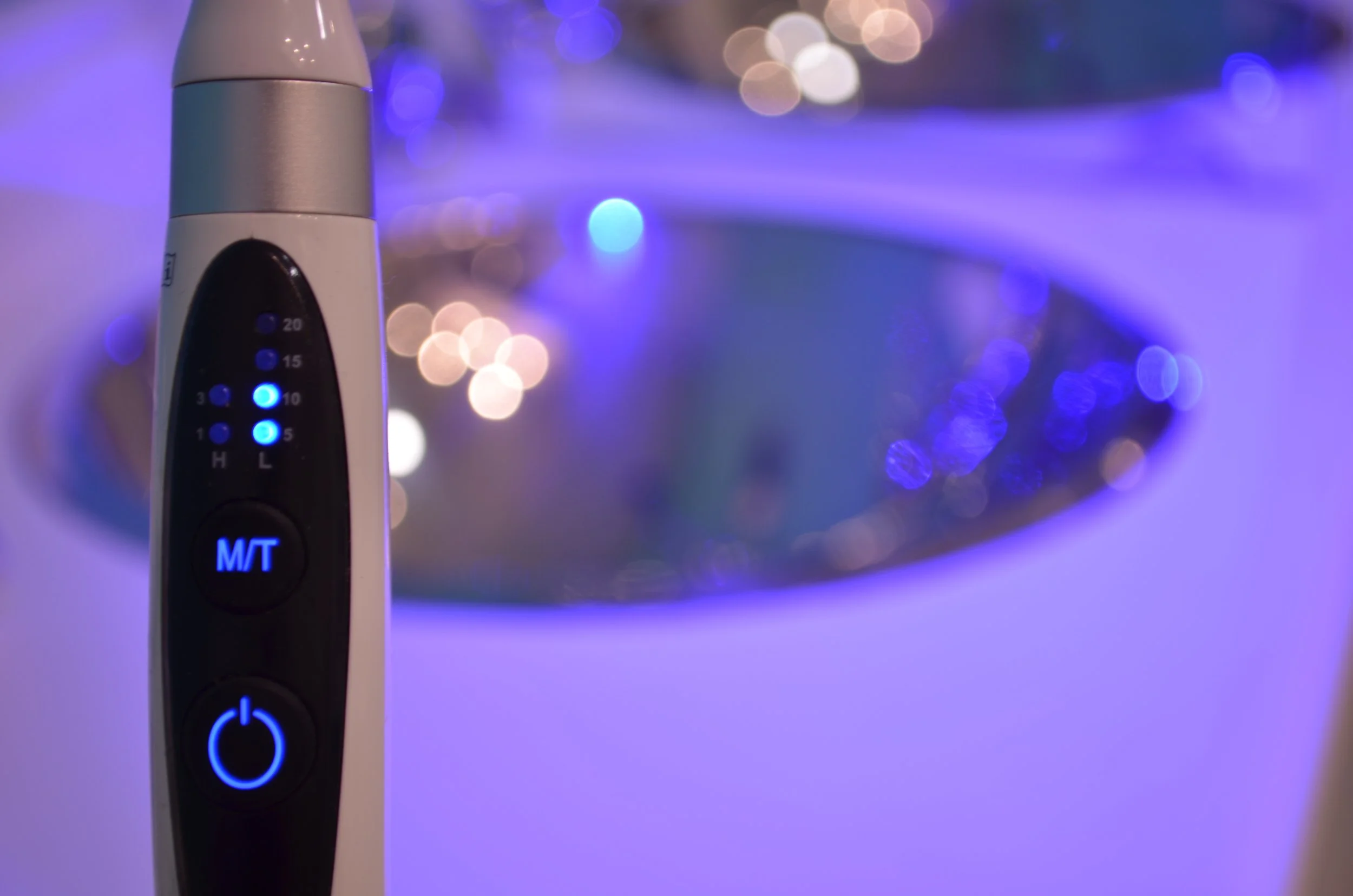 Un cepillo de dientes eléctrico con botones iluminados en azul y luz LED, en un fondo borroso con luces brillantes y difusas.