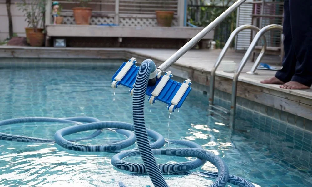 Limpia piscinas con aspiradora manual limpiafondos en una alberca en un patio exterior.