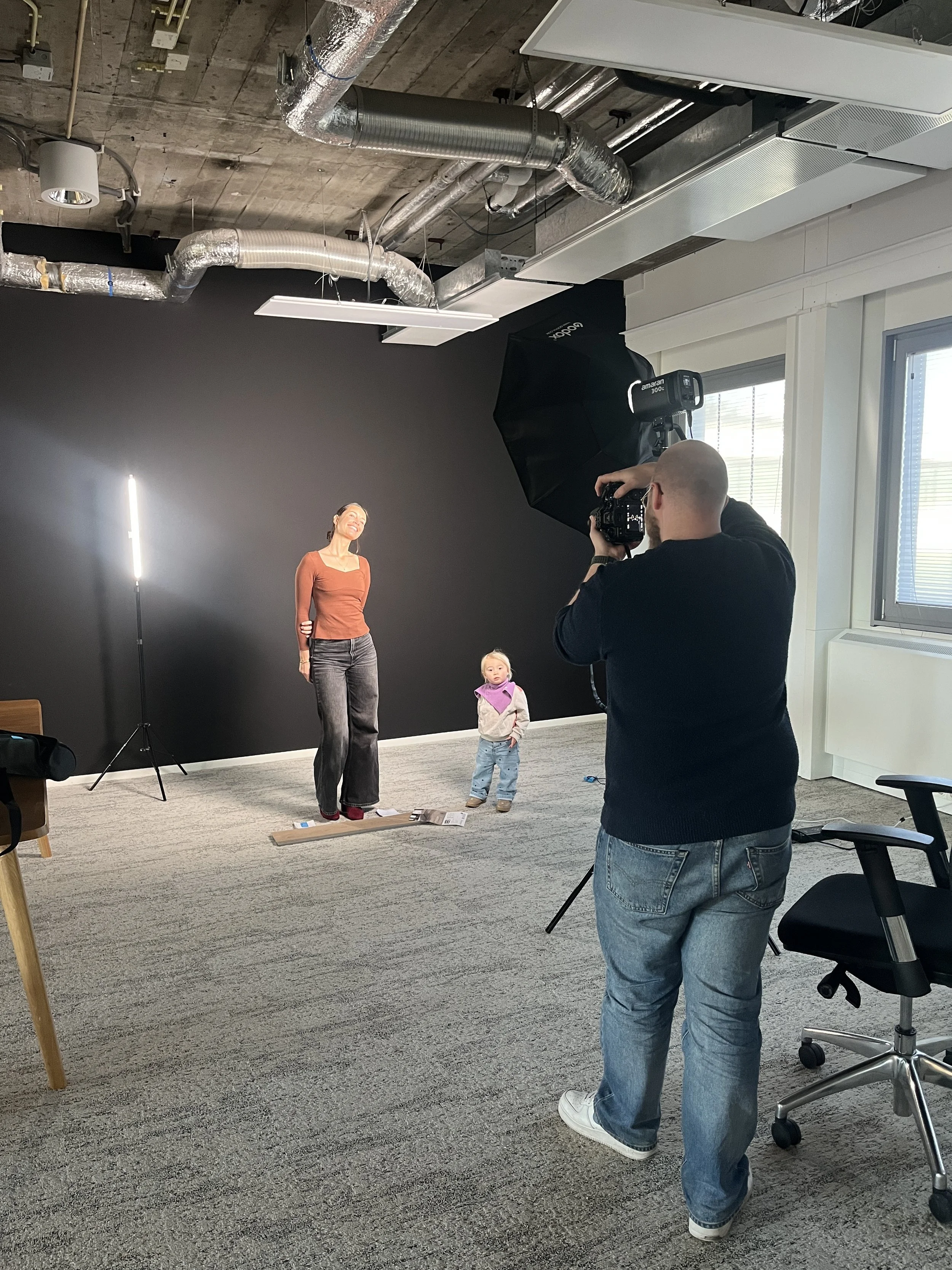 Fotograaf neemt foto's van een vrouw en een kind in een studio met een zwarte achtergrond, studioverlichting en ramen.