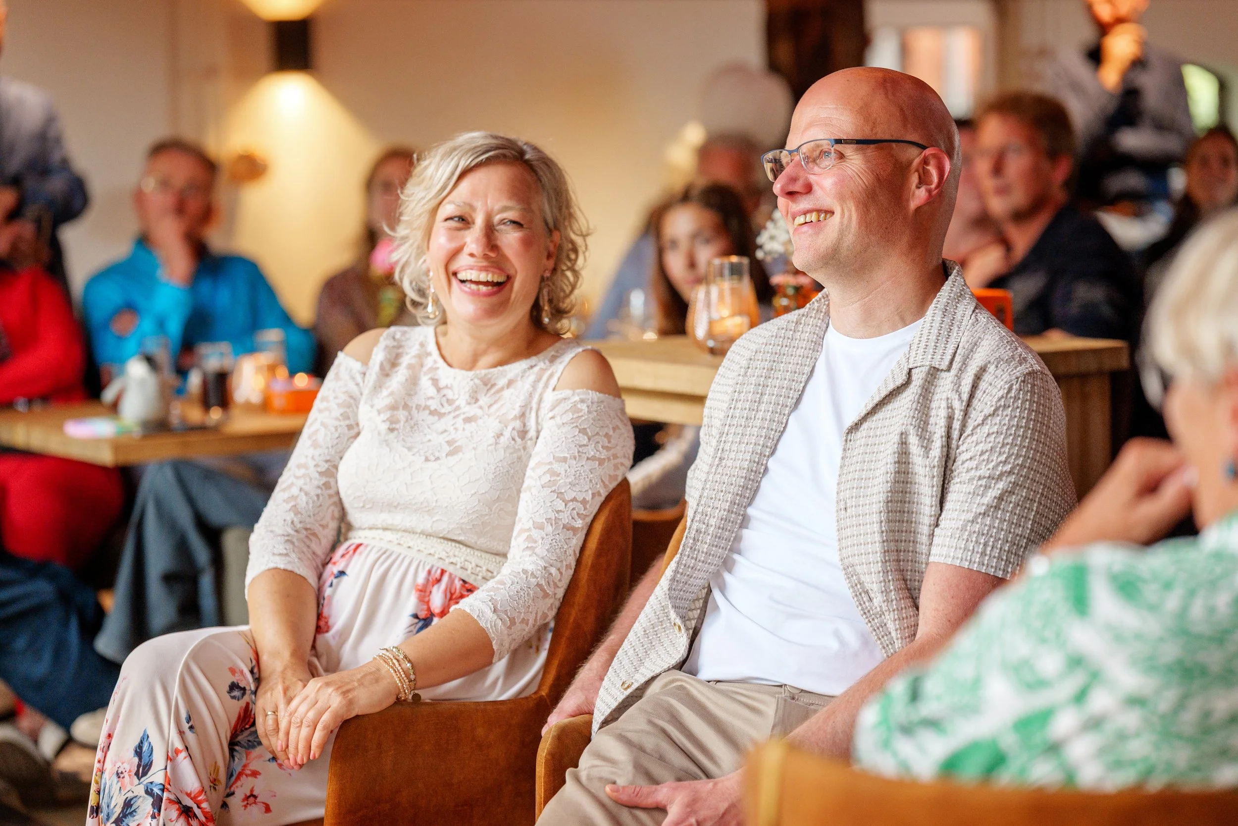 Mensen lachen en genieten tijdens een jubileum in een gezellige binnenruimte.Gefotografeerd door professionele jubileum fotograaf uit Nederland.