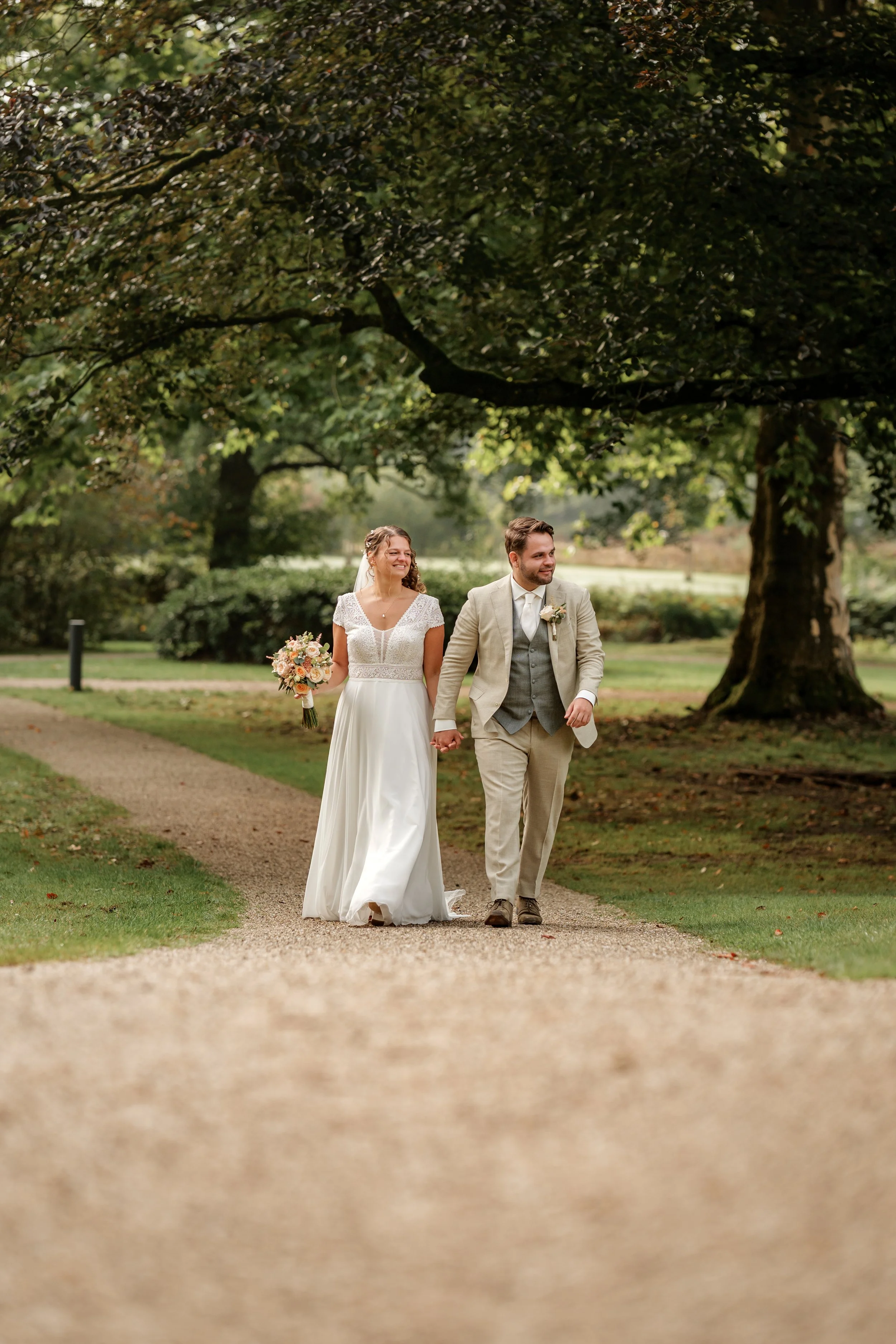 Spontane foto van een wandelend bruidspaar op een landgoed, voorbeeld voor het meest gekozen 'Klassiek' trouwpakket. Gefotografeerd door een professionele fotograaf uit regio Gelderland Nederland