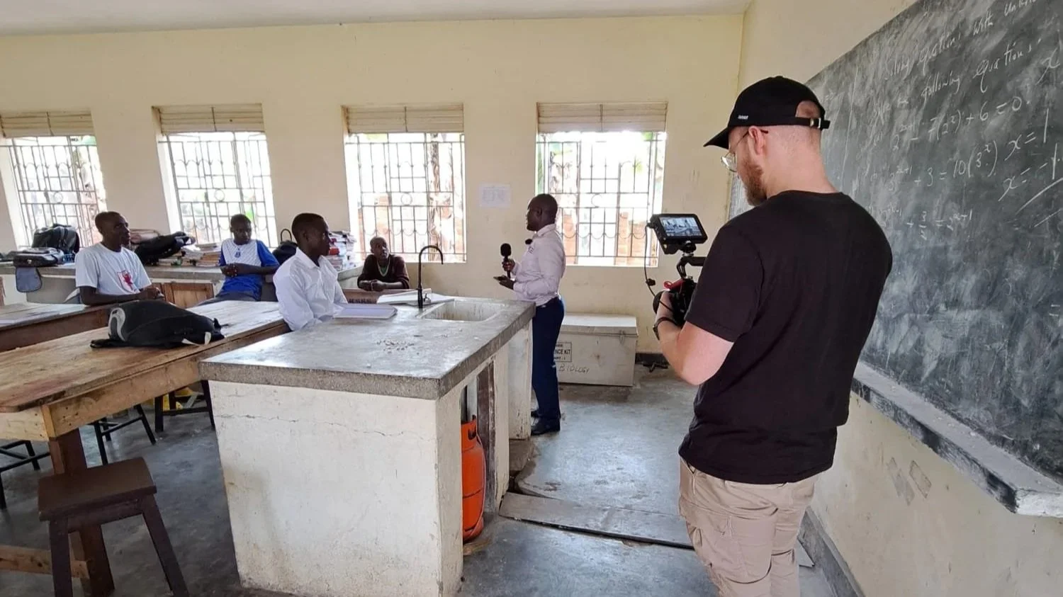 Een docent geeft les in een klaslokaal aan een groep leerlingen, terwijl een professionele en goedkope videograaf uit Gelderland met camera de les opneemt.