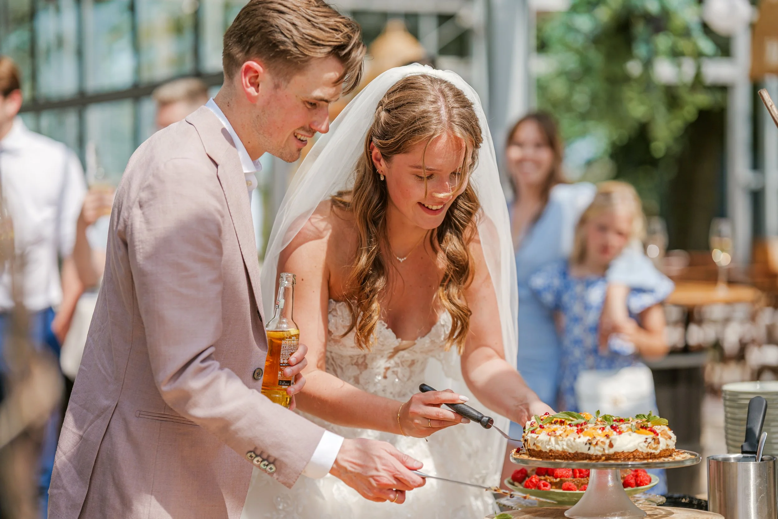 Een bruidskoppel snijdt een taart op een tuinbruiloft, omringd door gasten, gemaakt door professionele trouwfotograaf Gelderland