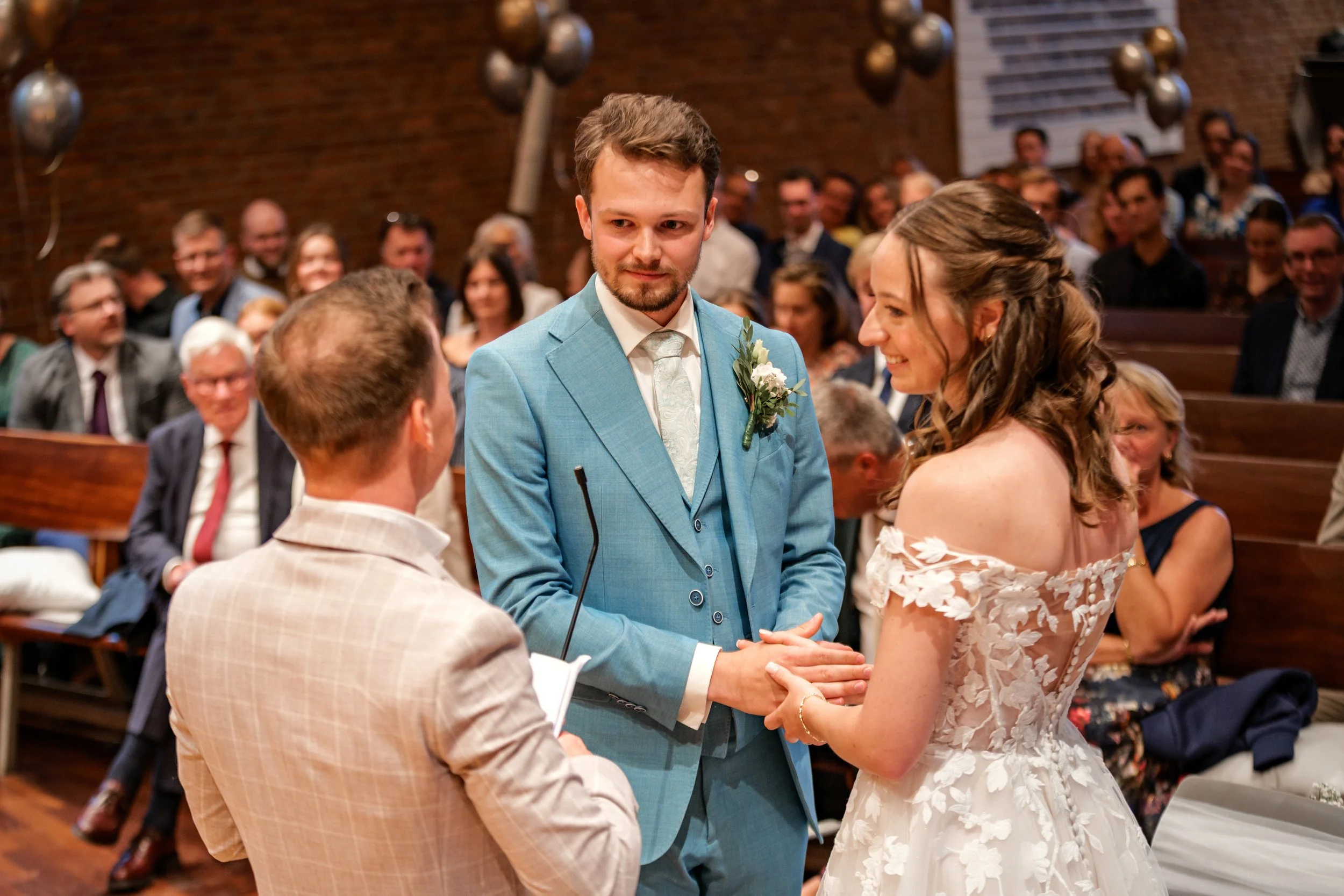 Bruidspaar houdt elkaars handen vast tijdens de trouwceremonie in de kerk, vastgelegd door een professionele trouwfotograaf