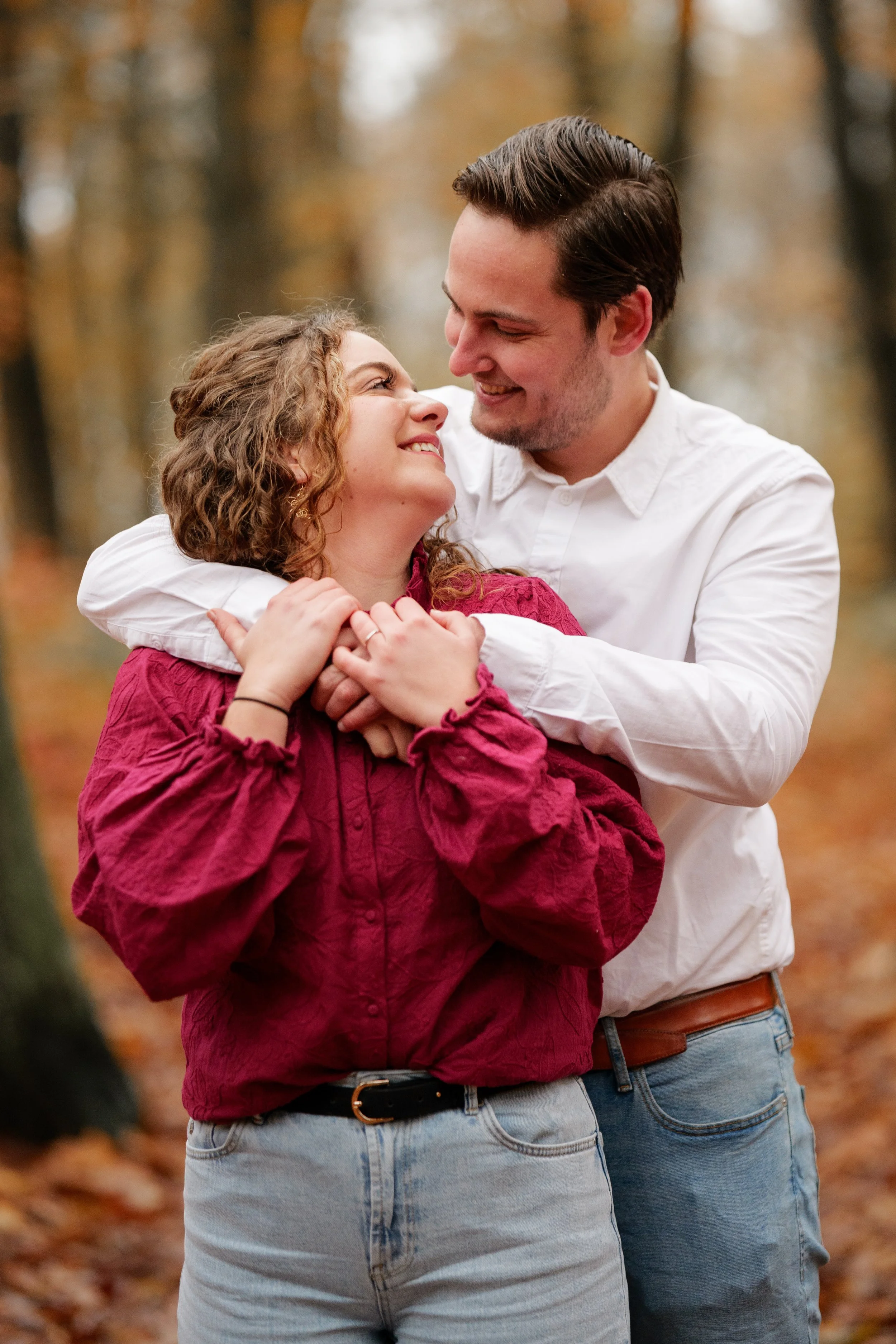 Een stel in een bos in de herfst, ze lachen en houden elkaar vast. Gefotografeerd bij mini shoot door professionele fotograaf uit Nederland.