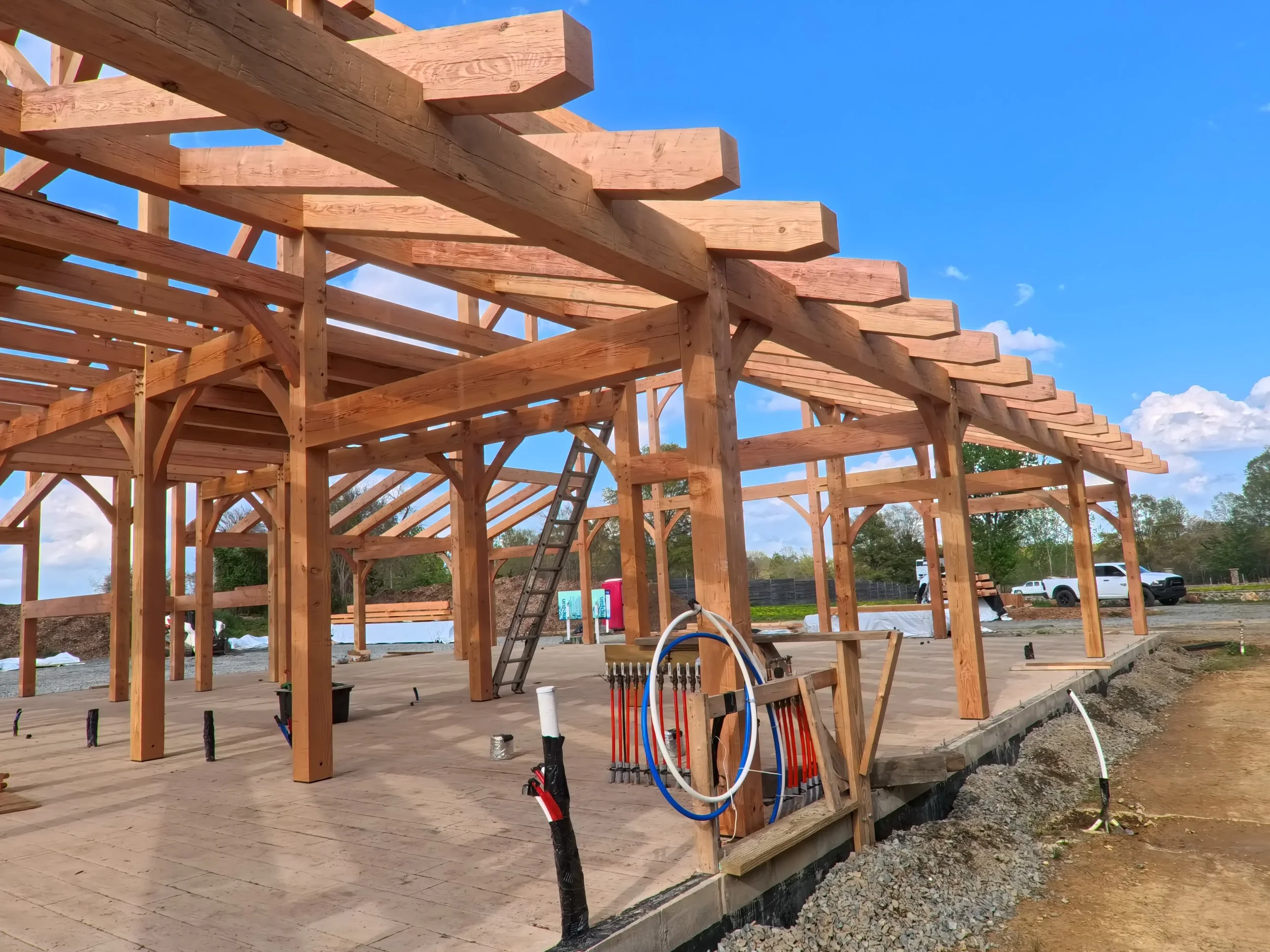 Construction site of a building with Douglas Fir Timber Frame, a ladder, and various construction equipment, under a blue sky with clouds.