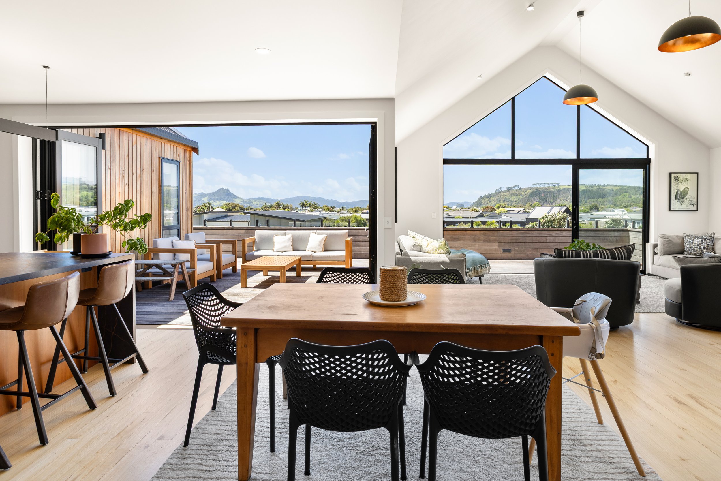 Open-concept living and dining area with large windows and sliding doors opening to a balcony with outdoor seating and scenic mountain views.