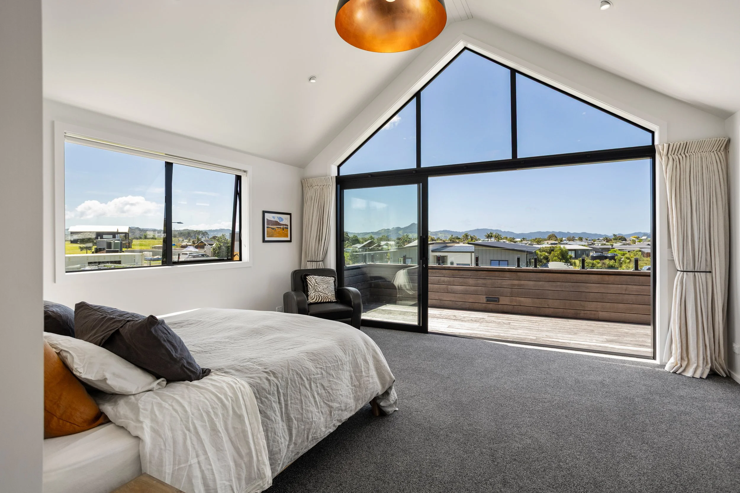 Modern bedroom with large window and balcony door showing a scenic view of mountains and homes outside.