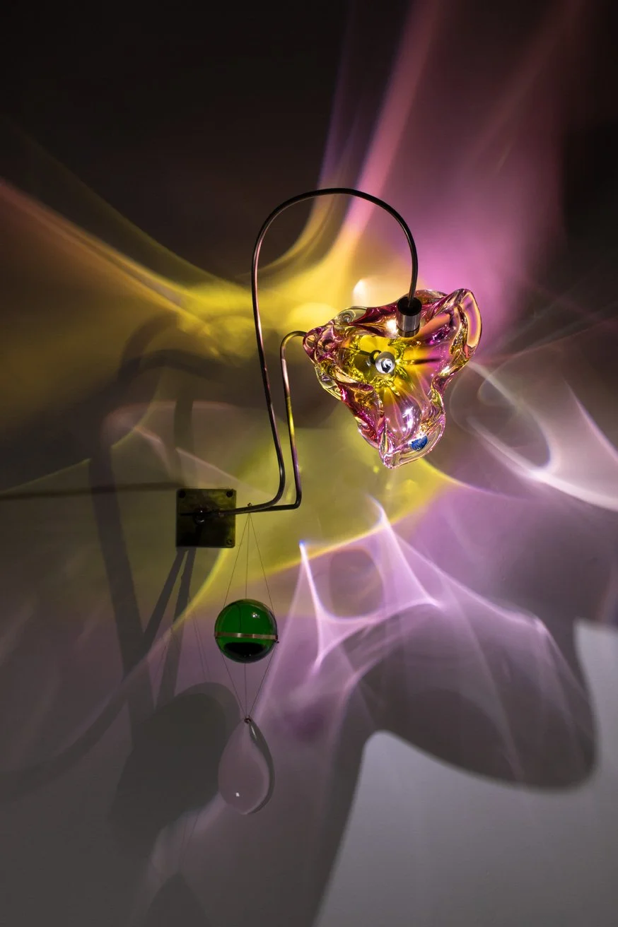 Glass art sculpture with colorful light reflections on the wall.