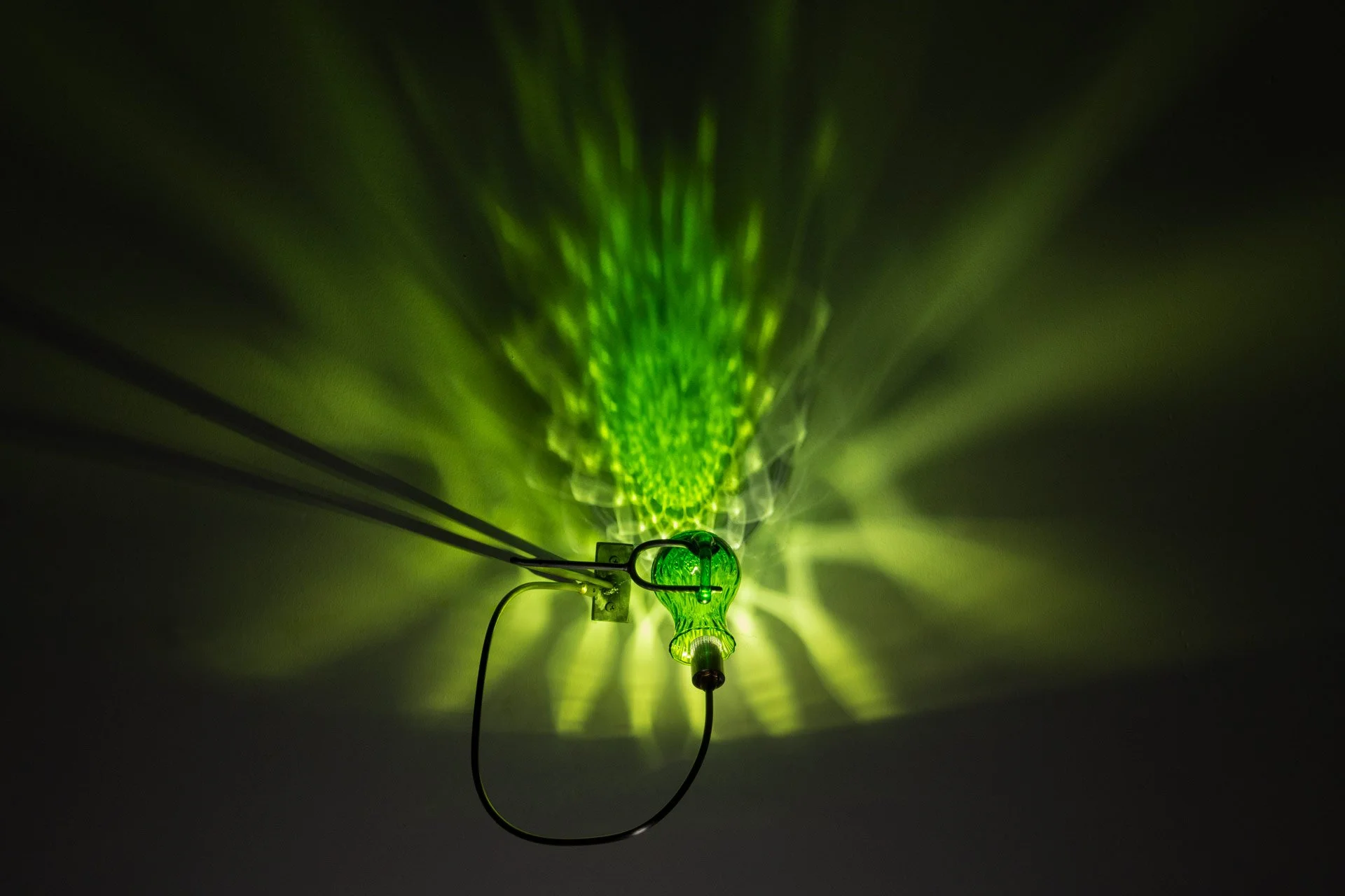Illuminated, wider view of the fixture displays green light in a mandala-like pattern.