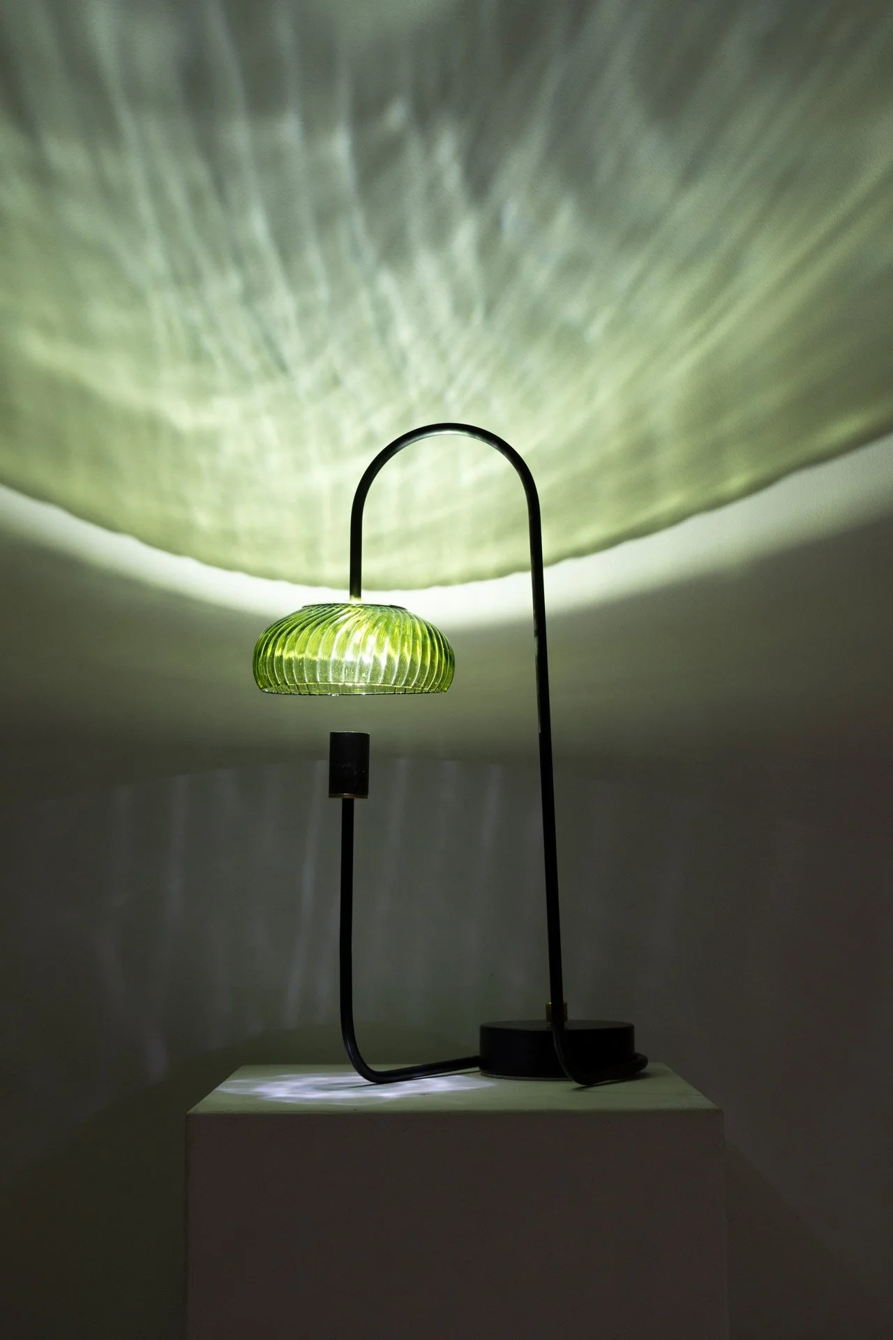 Illuminated, wider view of the lamp on a table displays green light in a textured pattern.