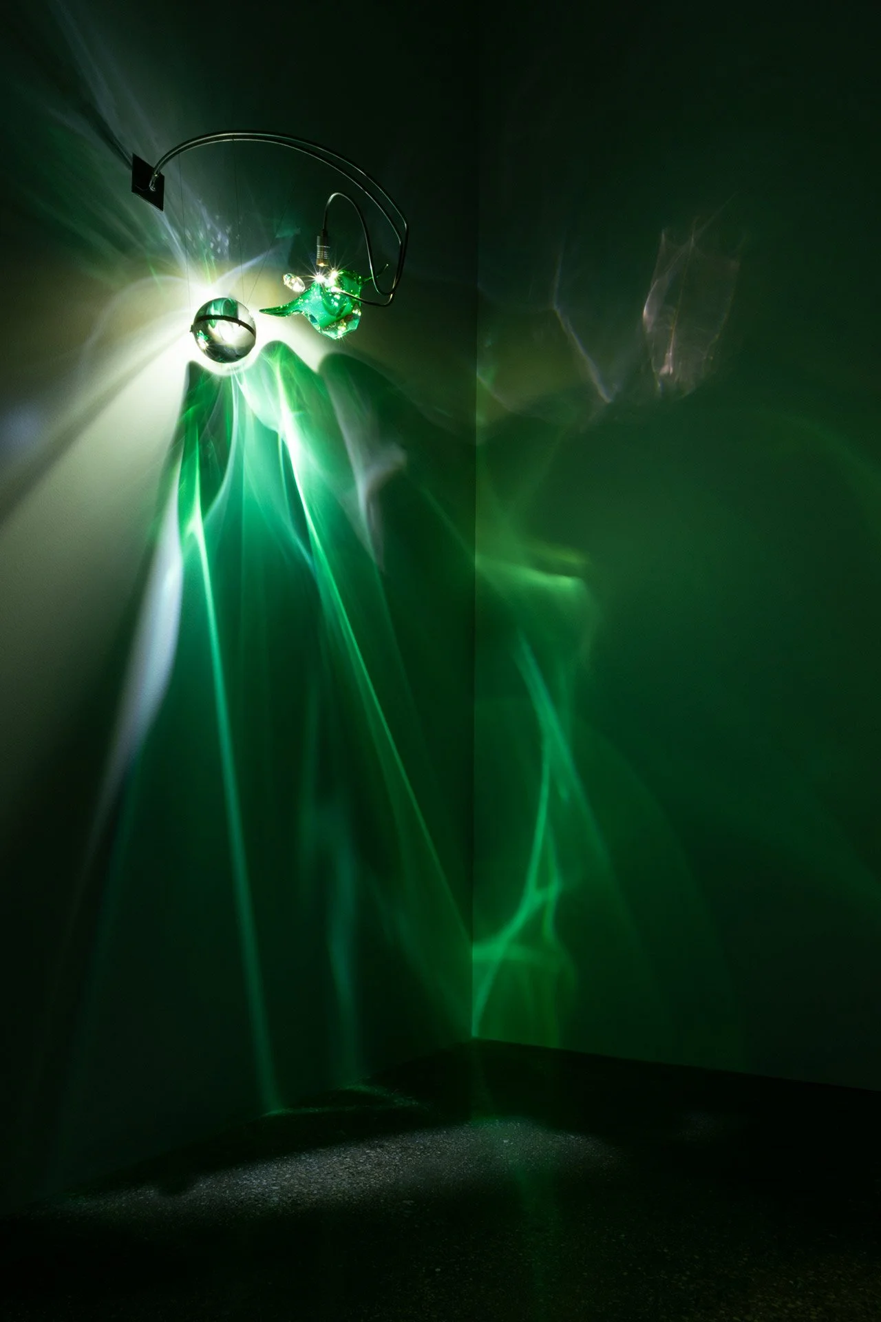 Illuminated, wider view of the fixture displays green and white light in a complex geometric pattern.