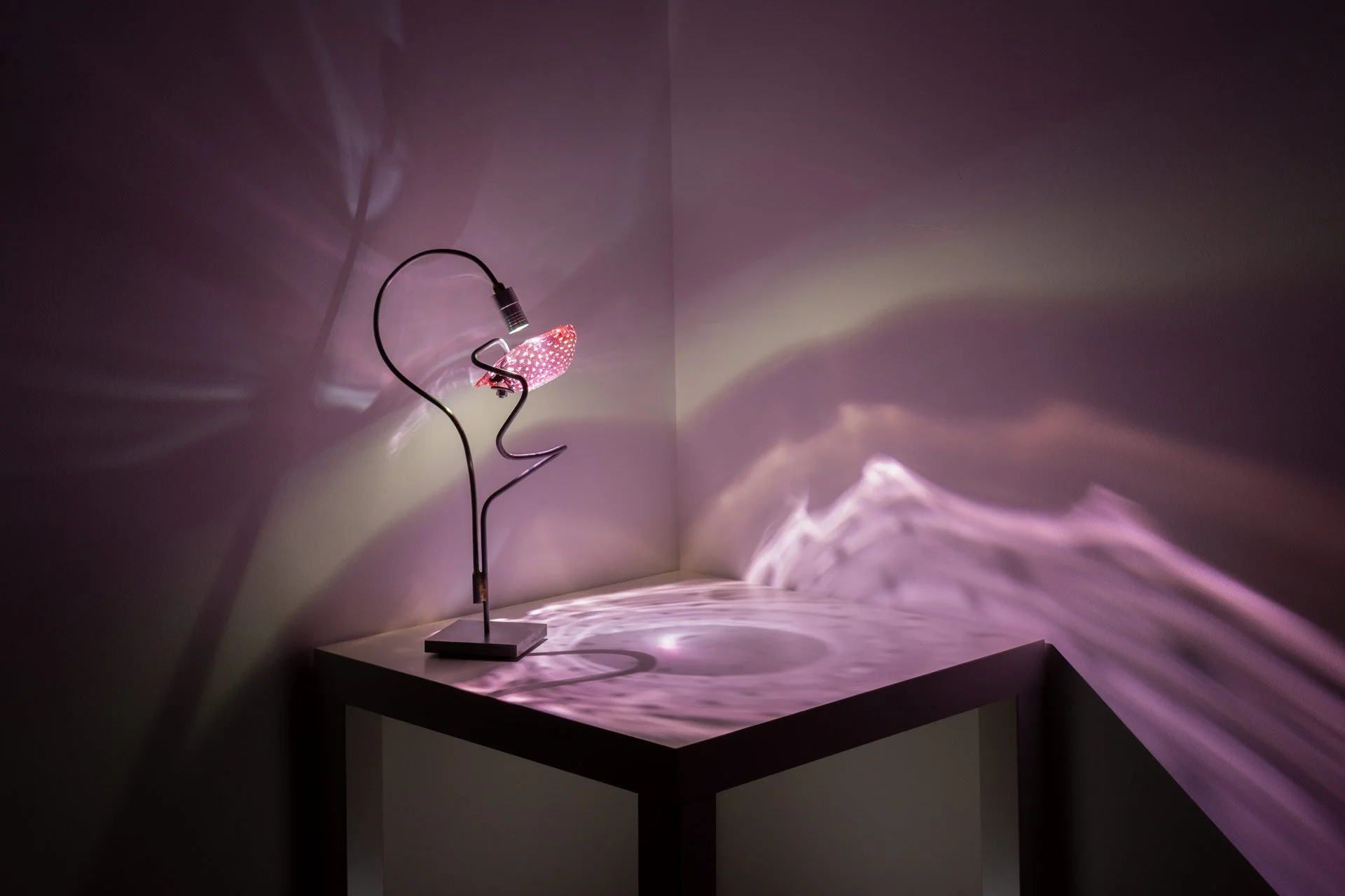 Illuminated, wider view of the lamp on a table displays textured pink and white light.