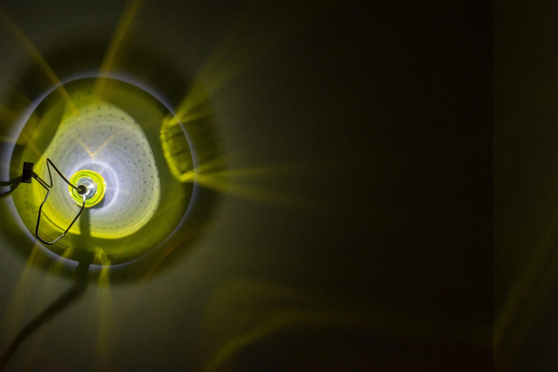 Illuminated, wider view of the fixture displays layered yellow and white light that forms a circle on the wall it’s mounted on.
