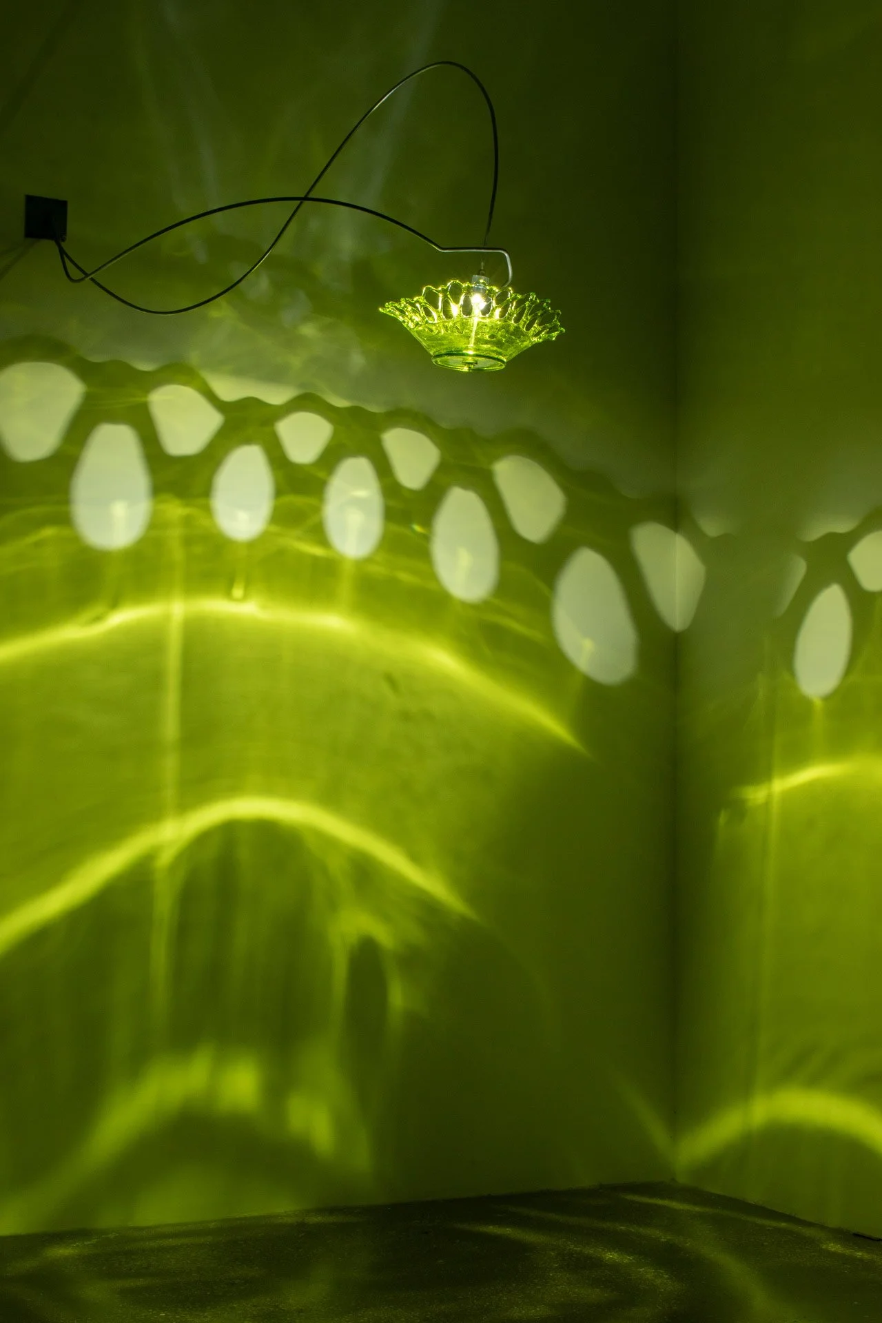Illuminated, wider view of the fixture displays green light with a lace pattern.