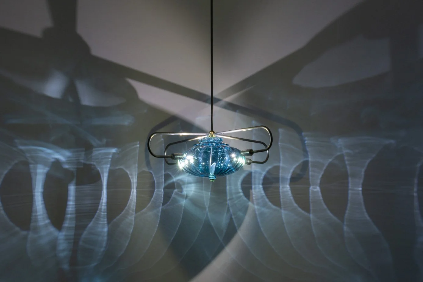 A modern ceiling light fixture with blue glass and multiple small bulbs, casting intricate light and shadow patterns on the ceiling.