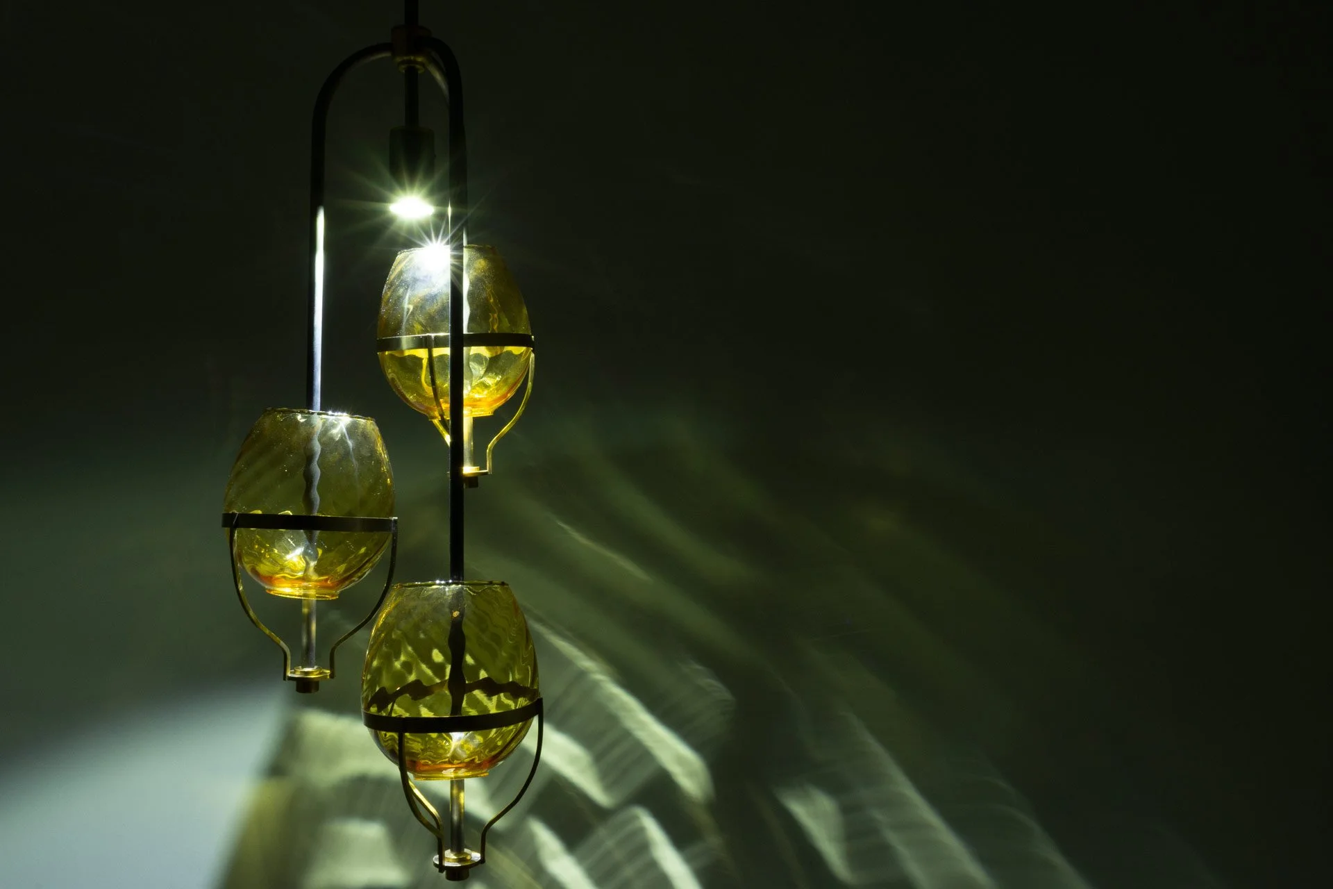 Illuminated detail shot of the three lampshades, highlighting the quality of the glass that leads to a unique light cast.