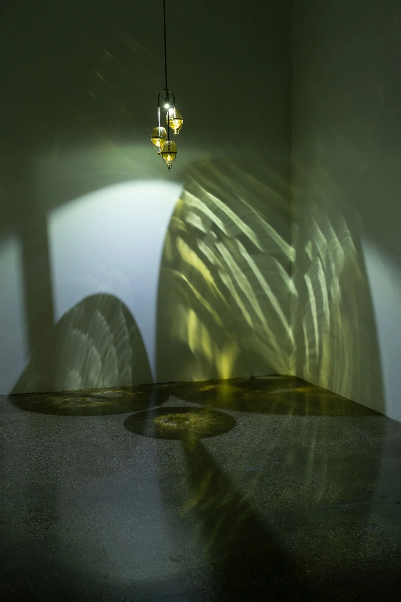 Illuminated, wider view of the fixture displays three distinct circles of swirled yellow light.