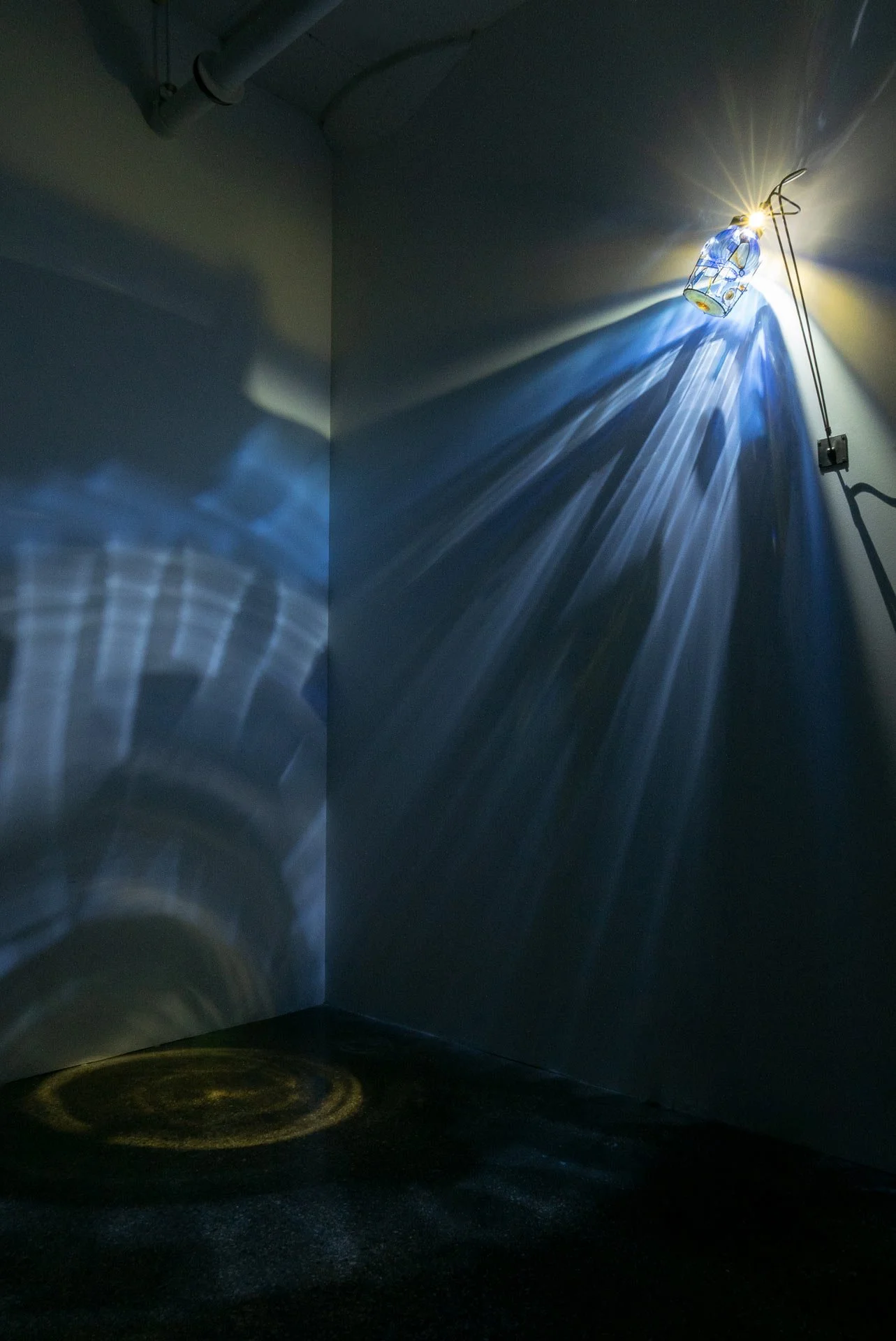 Illuminated, wider view of the fixture displays blue light and a yellow circle of light that hits the floor.