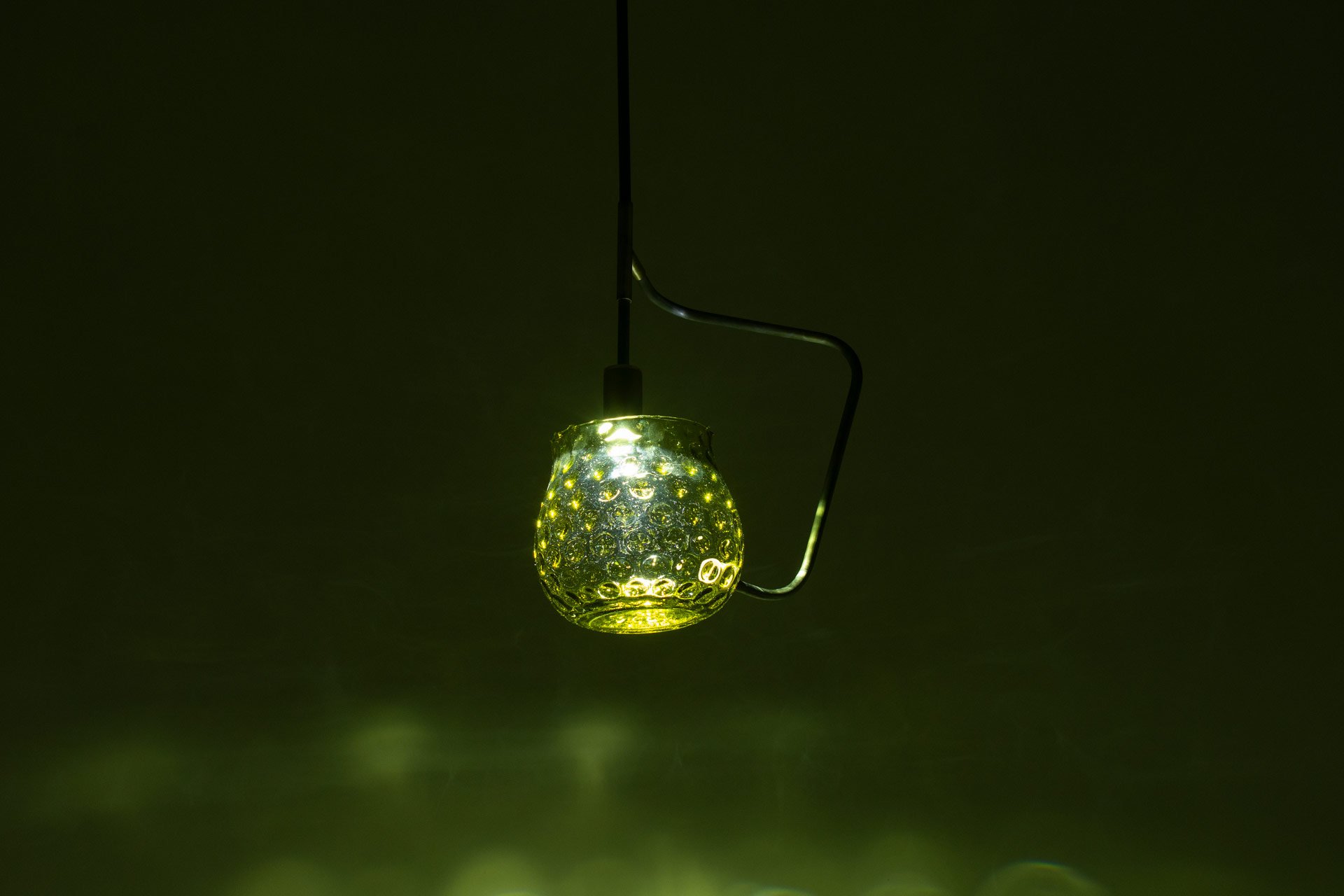 Ceiling pendant fixture made of bent steel piping, brass accents, and a green vintage dimpled glass vase. LED-lit, it casts green, water-like light.