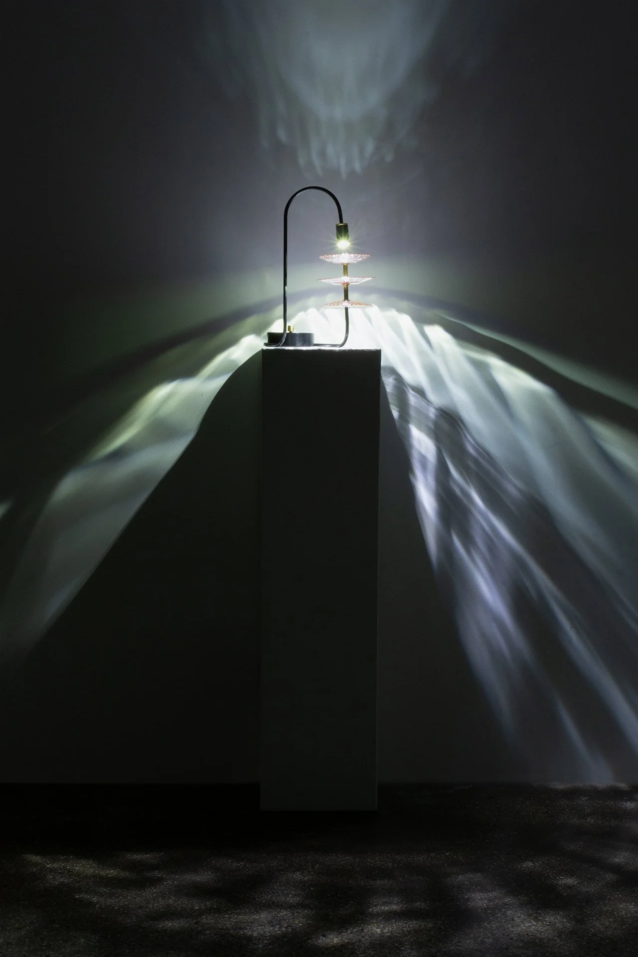 Illuminated, wider view of the lamp on a table displays white light in a ribbed, ethereal pattern.