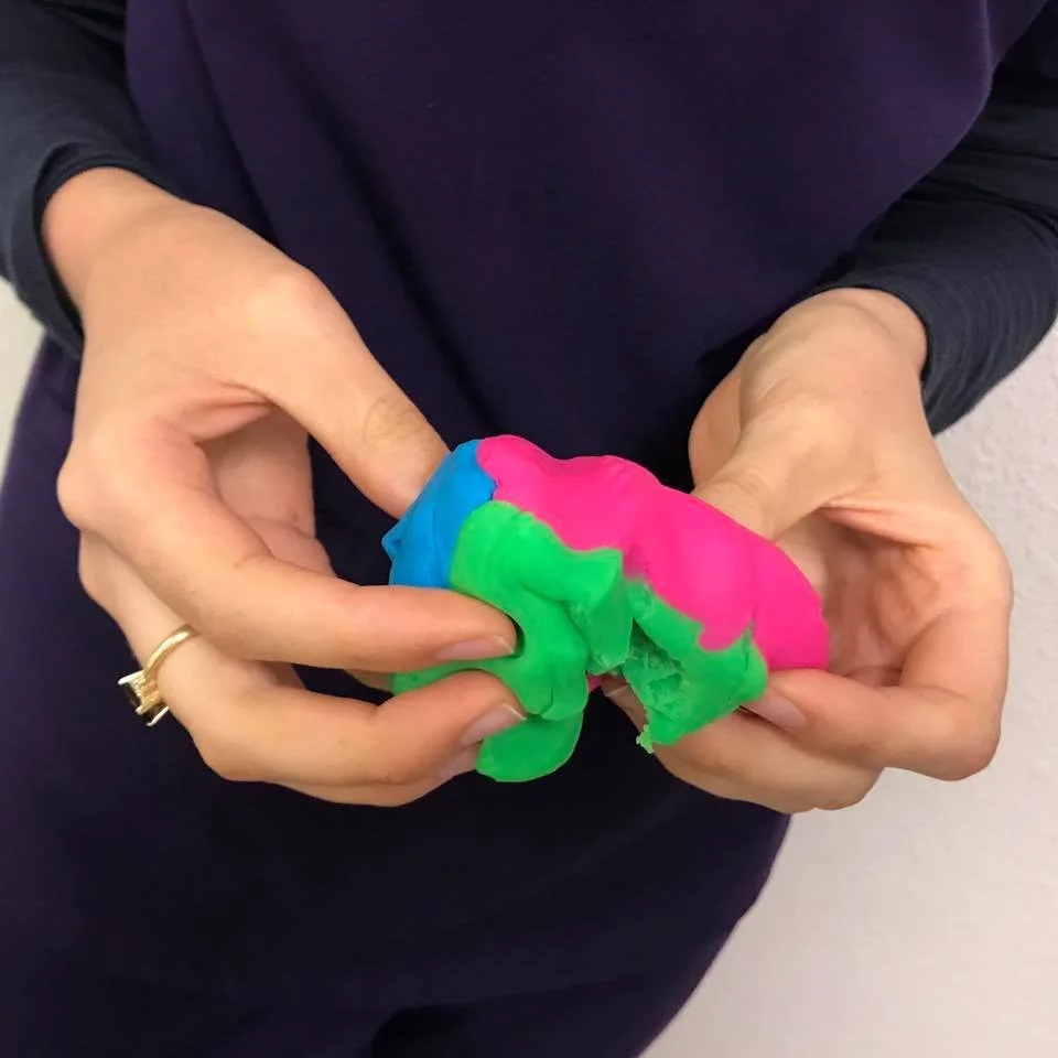 Person holding a colorful piece of slime in pink, green, and blue colors.