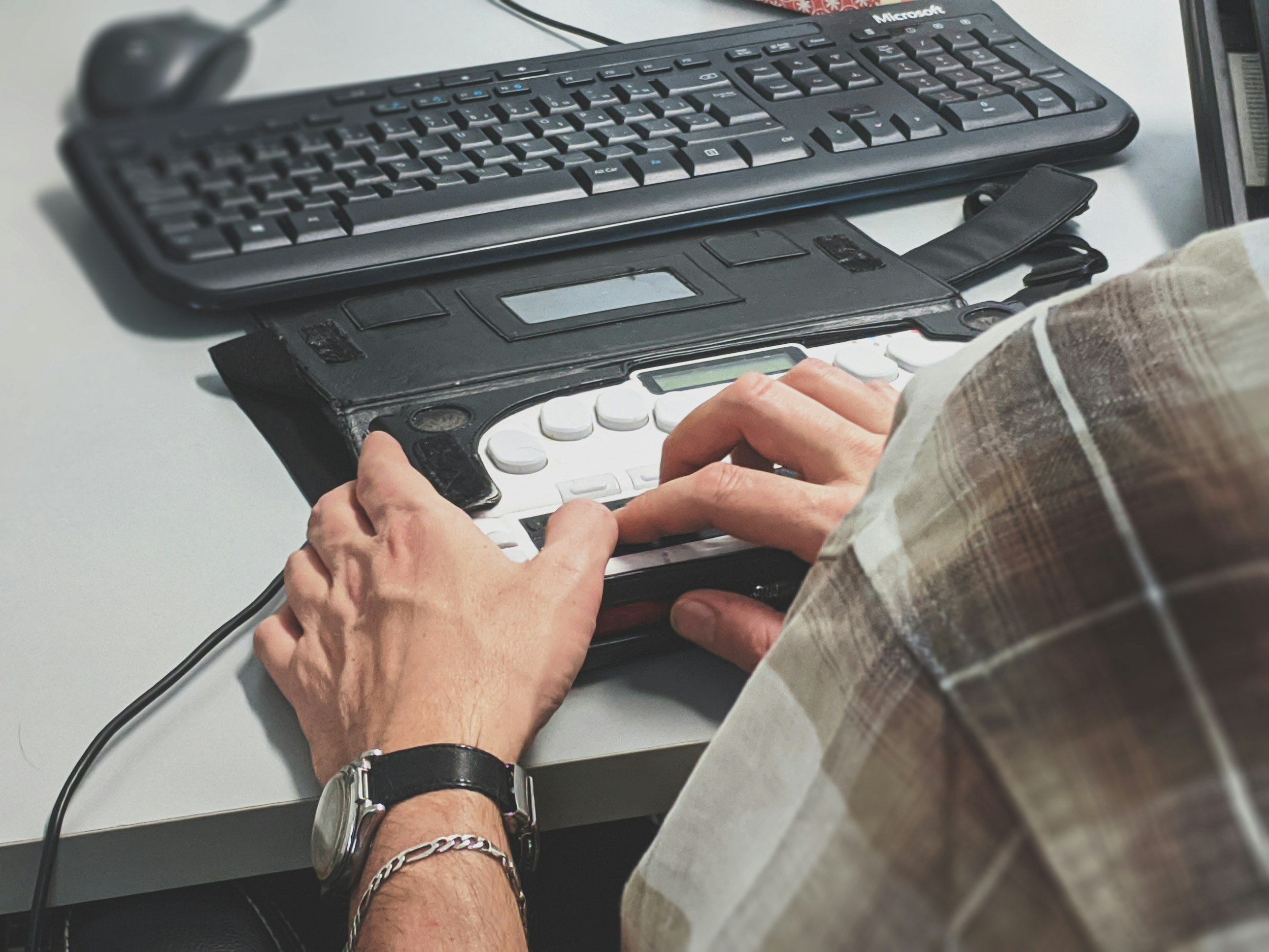 Person working on a Braille translation device at a desk with a computer keyboard nearby.