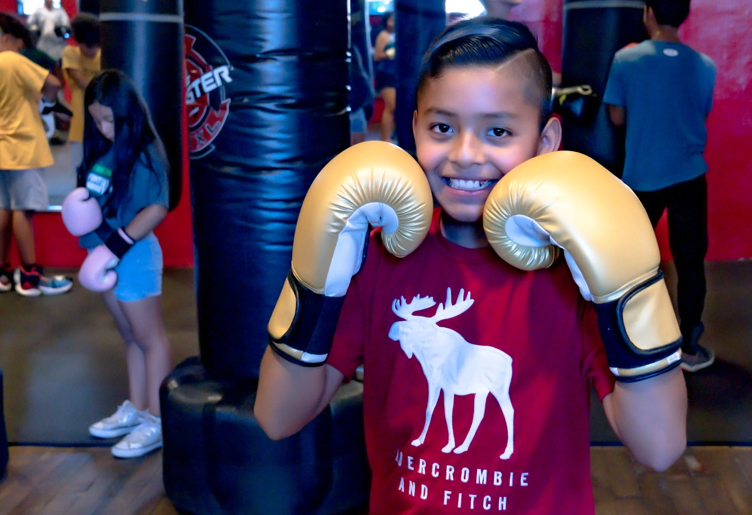 Young boy smiling with boxing gloves at NJGAKAD youth boxing program at Gleason's Jersey Shore