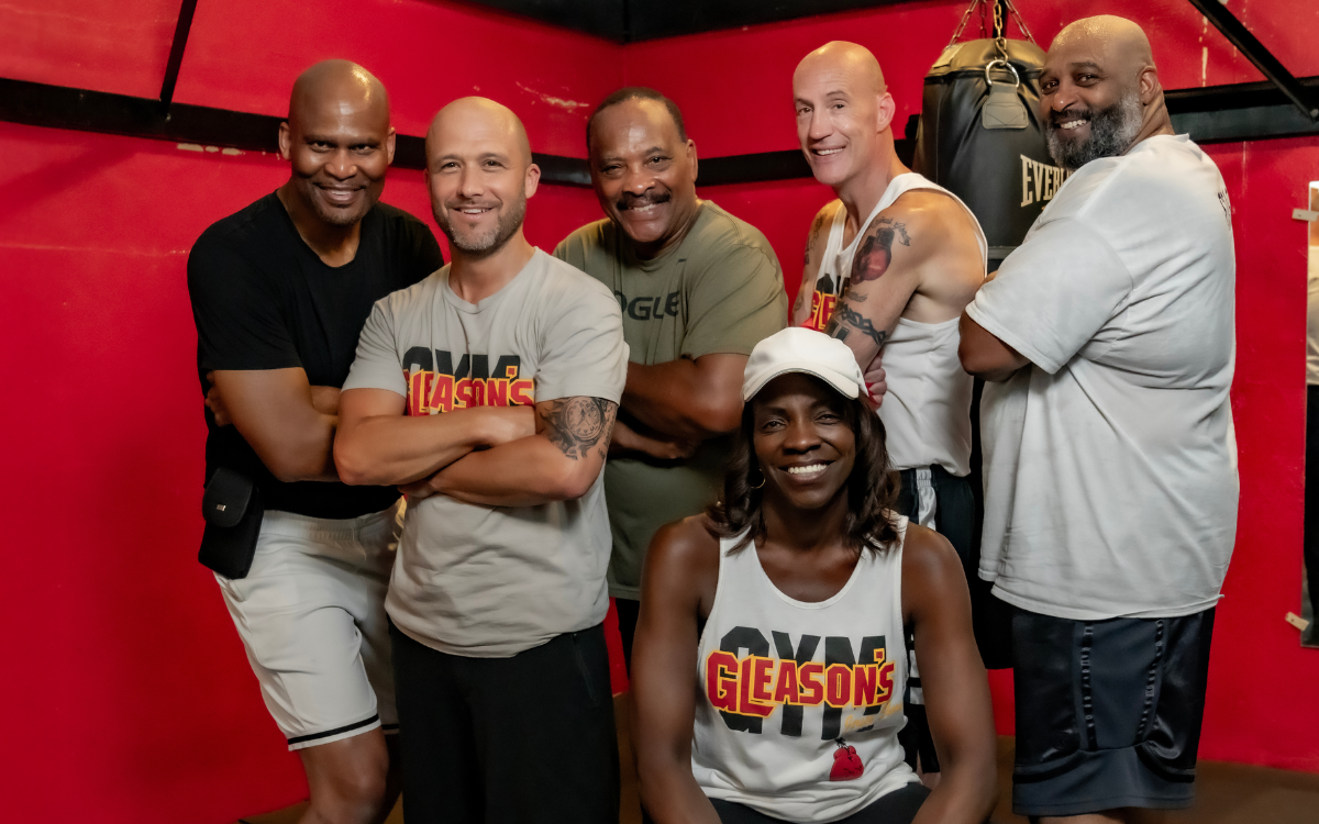 "Gleason's gym coaching team and trainers posing together in front of red and black boxing ring